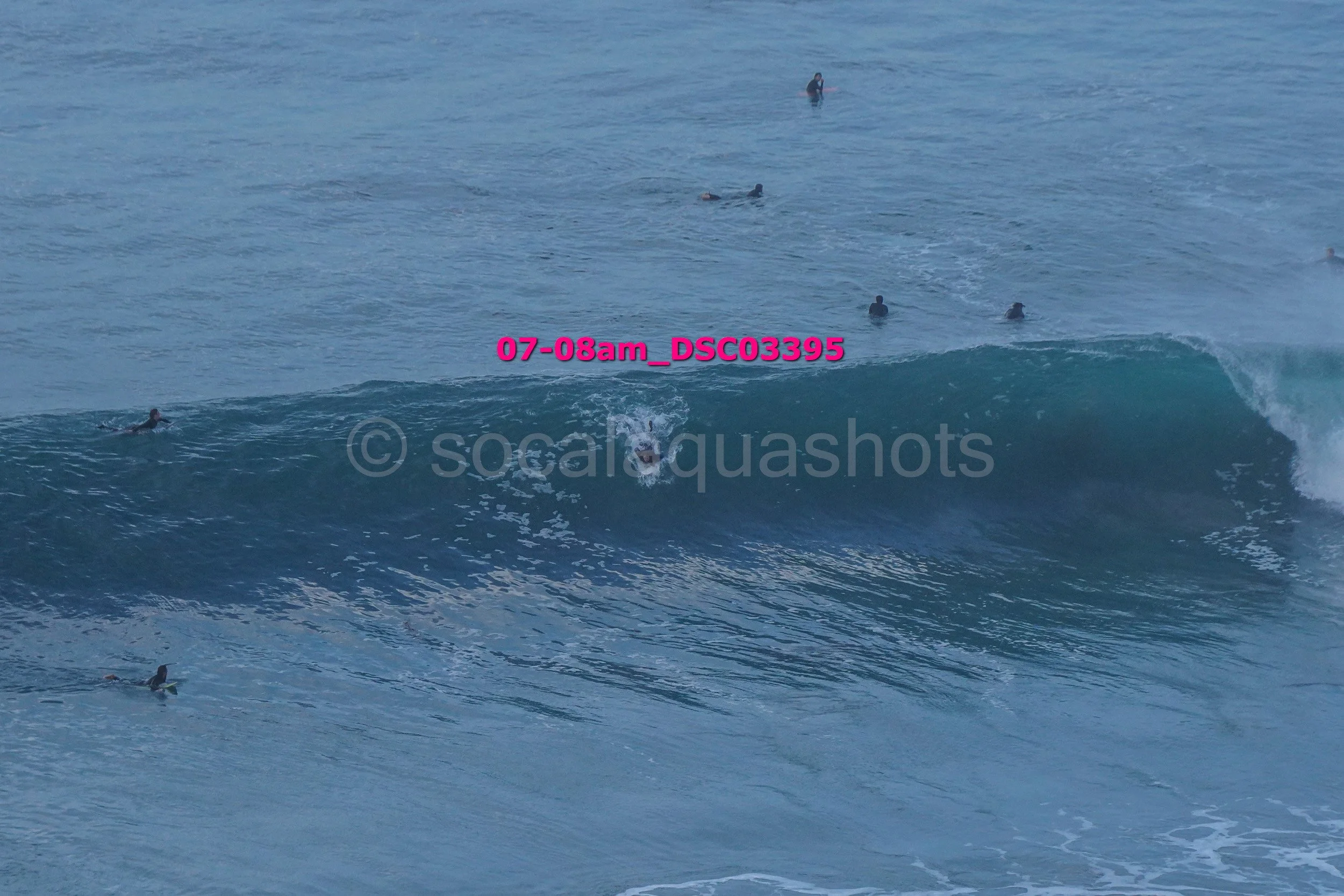 People surfing on a wave in the ocean with some swimmers in the background.