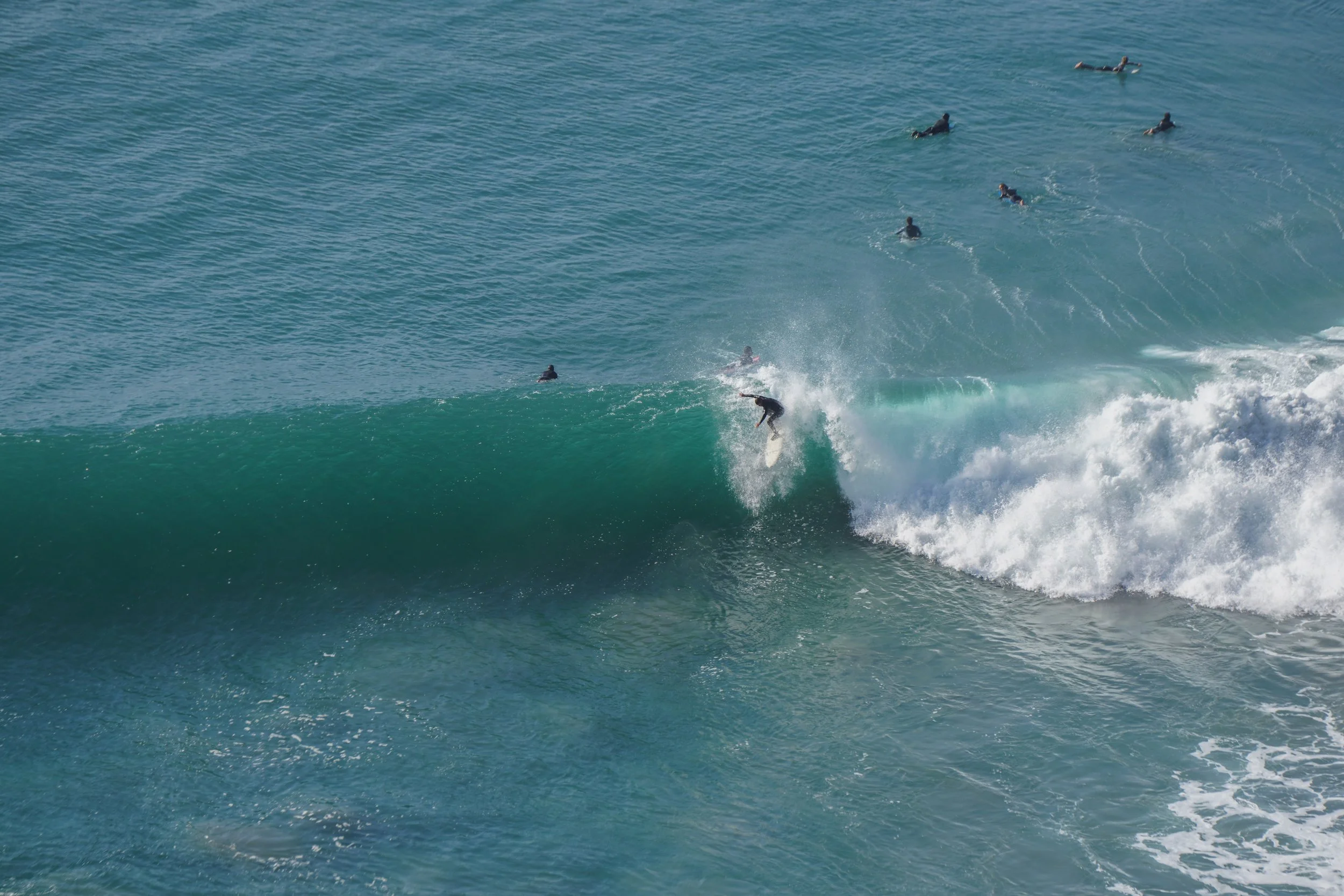 Surfer riding a wave with multiple surfers in the background in the ocean.