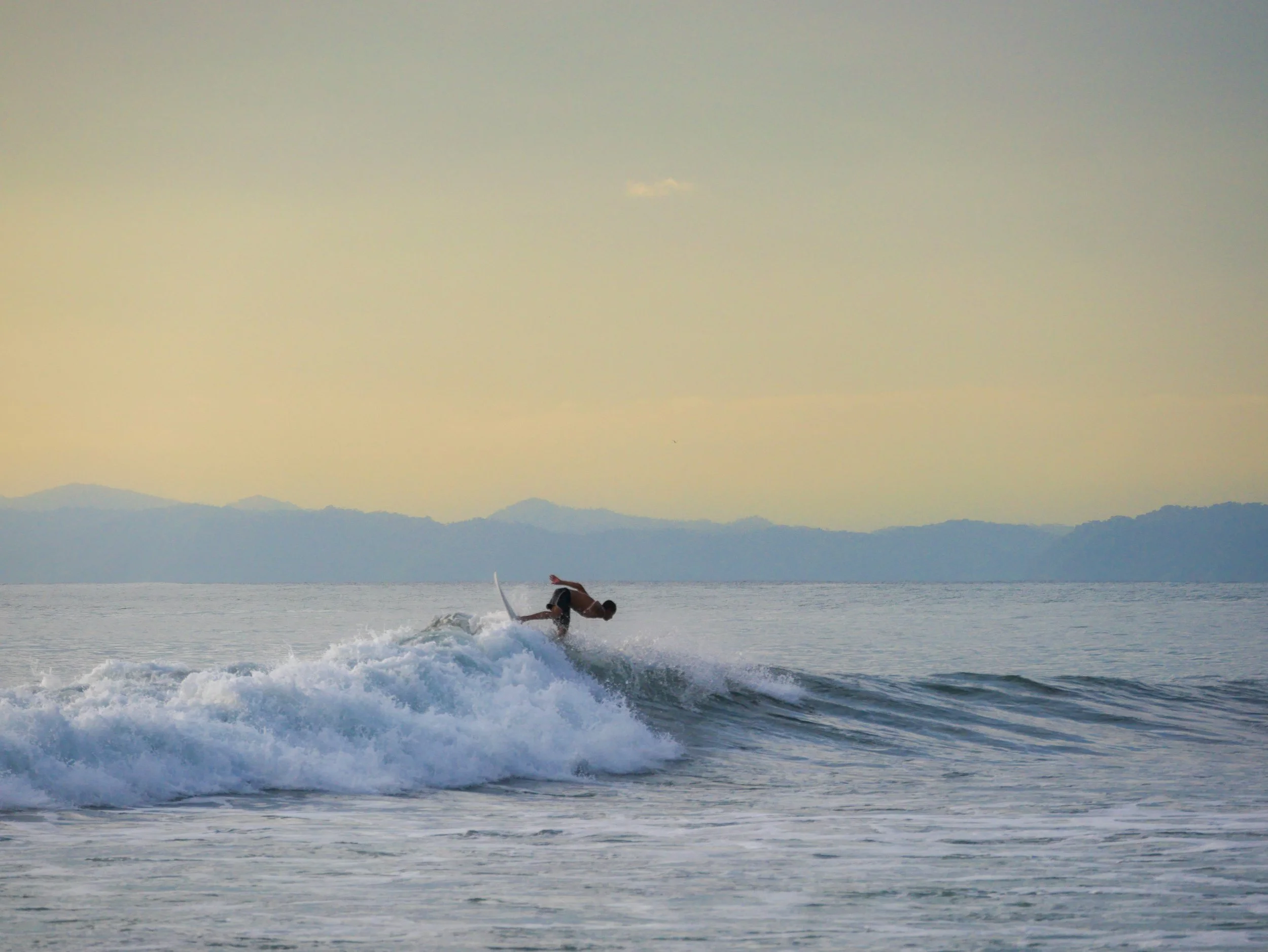 Surfer riding a wave at sunset with mountains in the background
