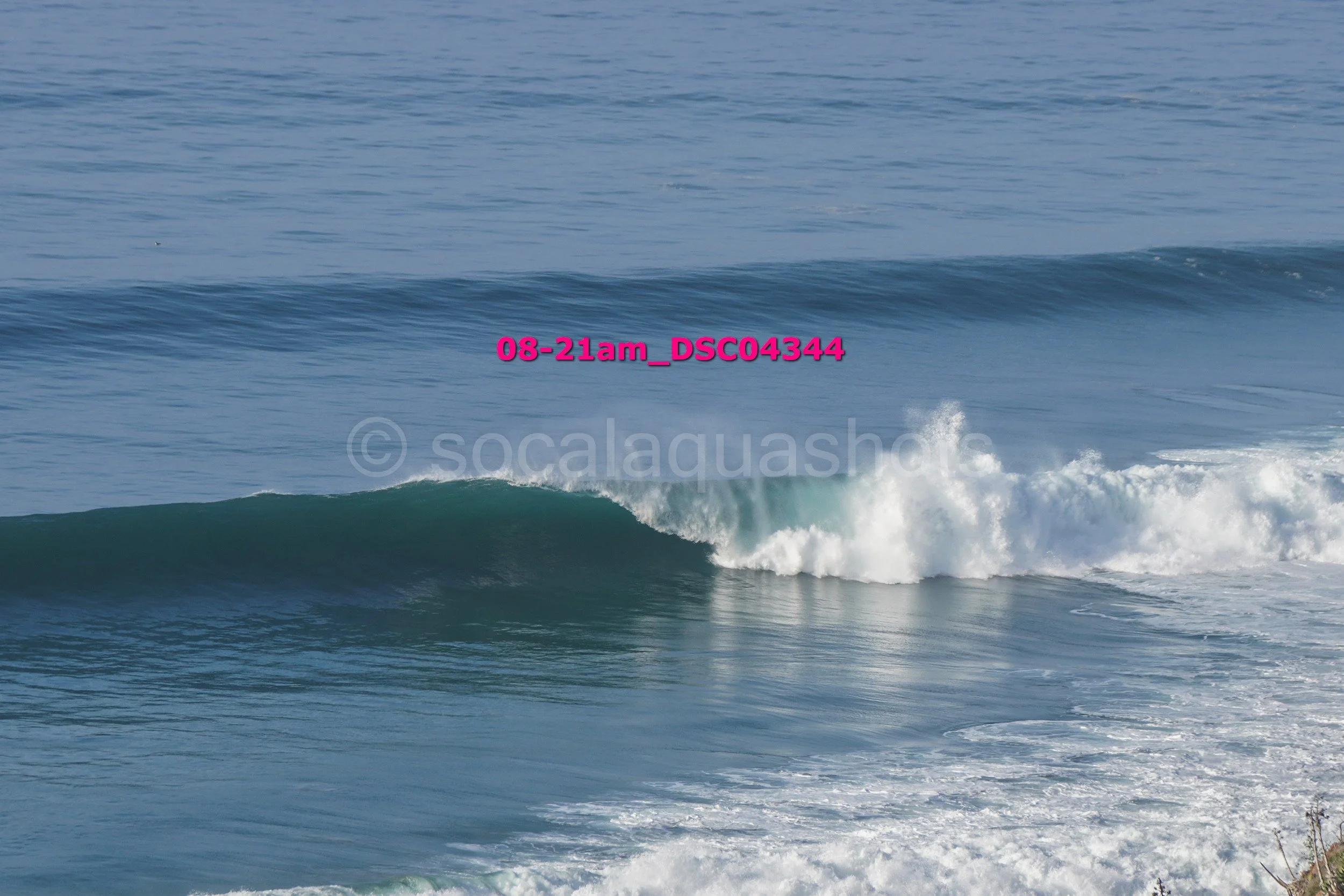 Ocean waves with a small wave breaking in the foreground and a larger, rolling wave in the background.