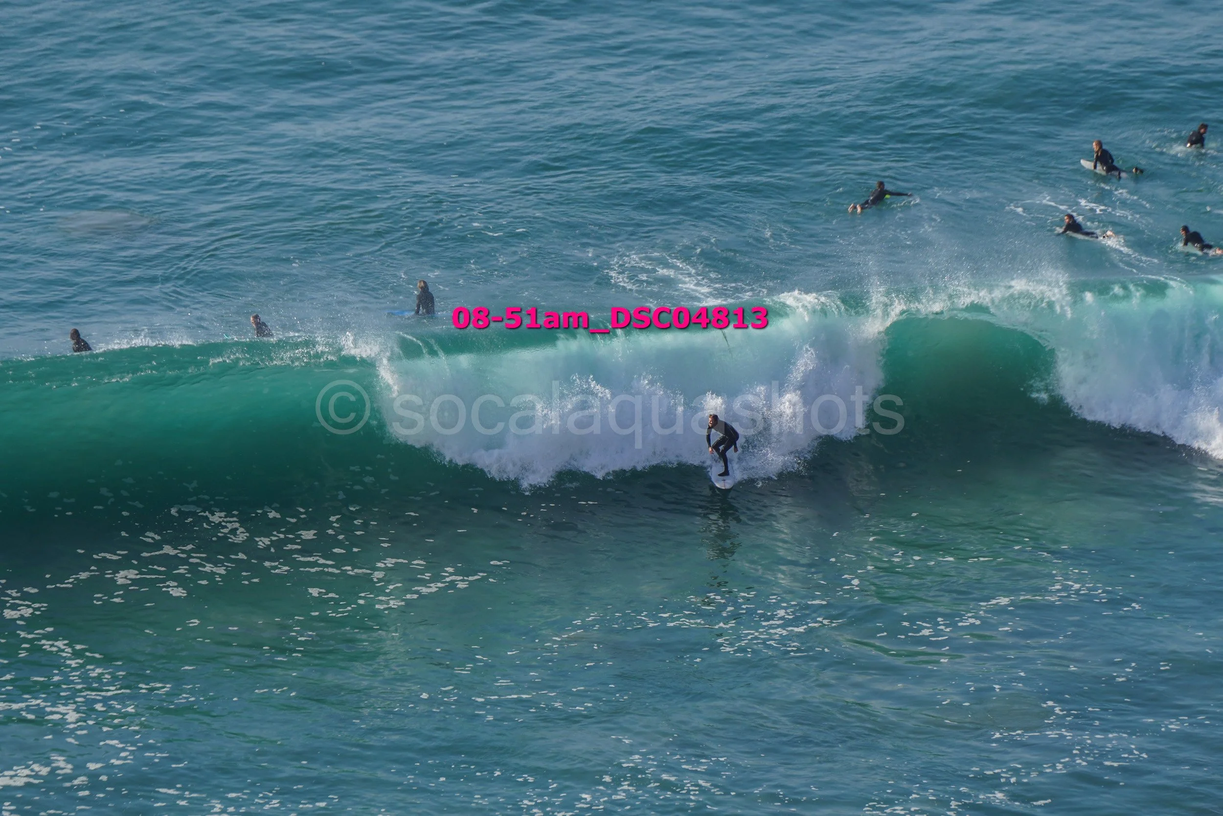 A person surfing on a large wave with several other surfers in the water behind them.