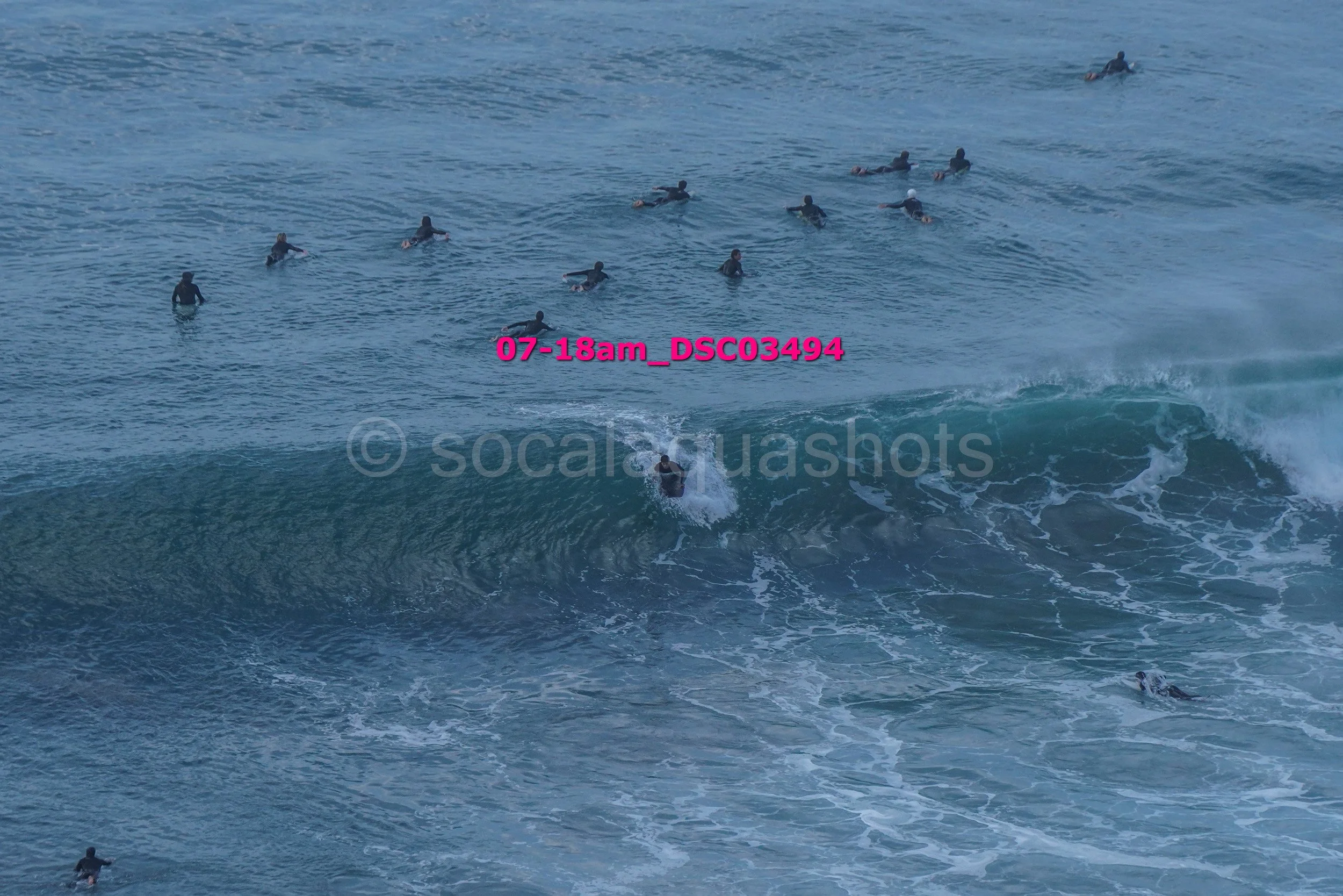 Surfers in the ocean, some on surfboards, some riding a wave, others waiting in the water.