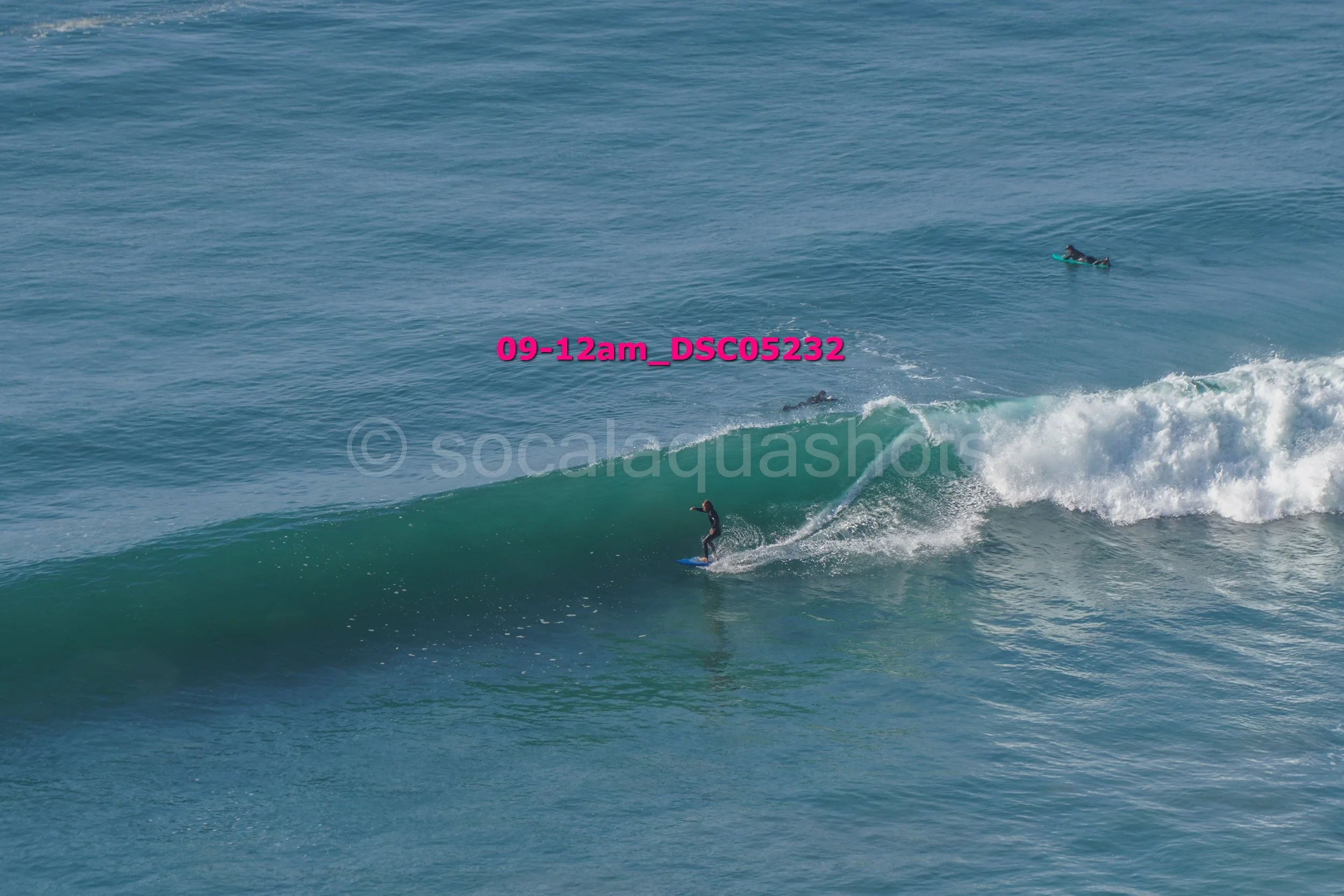 A person surfing on a wave in the ocean with two other surfers in the background.
