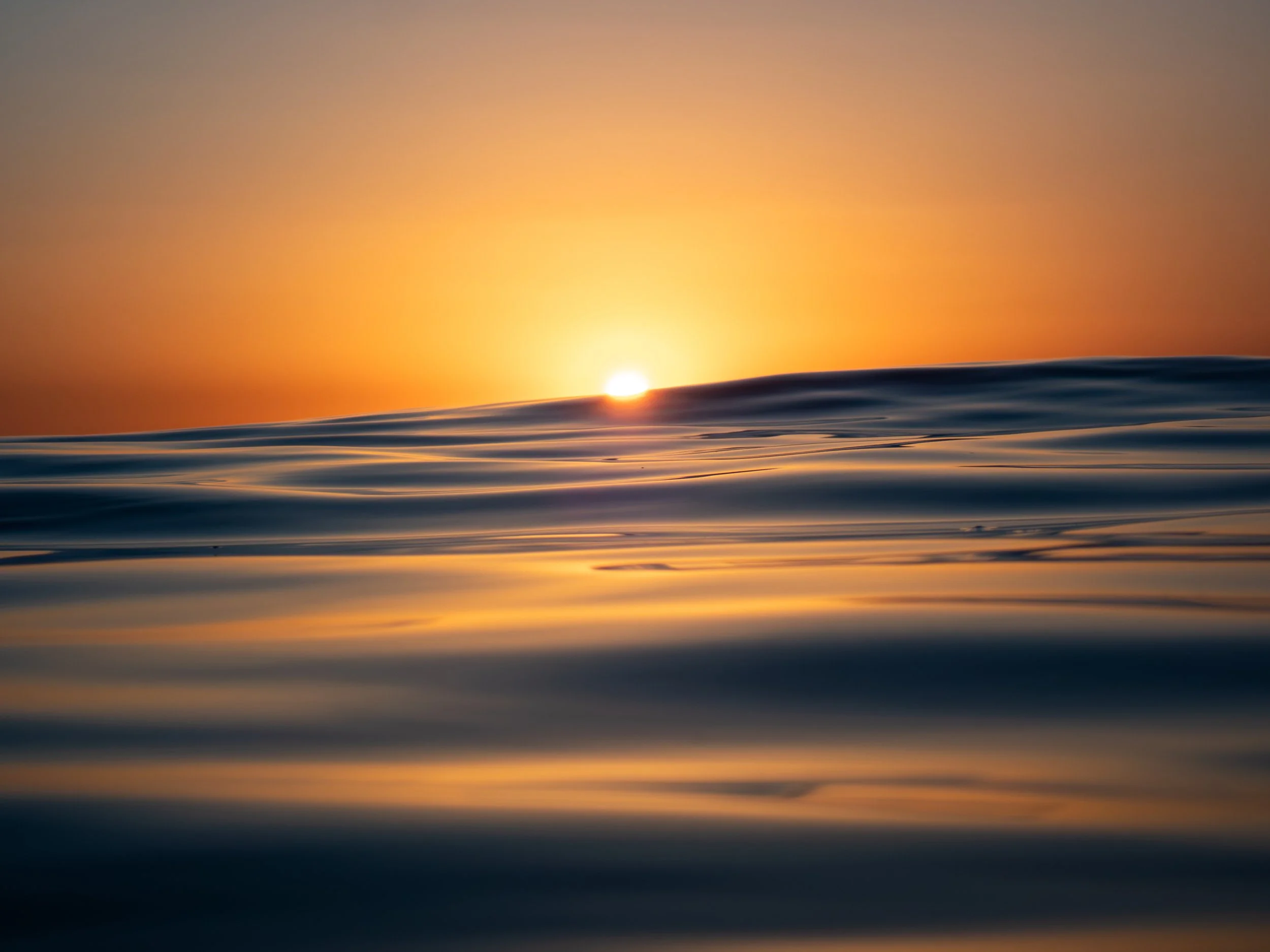 Sunset over the ocean with calm waves reflecting the sky's warm colors.