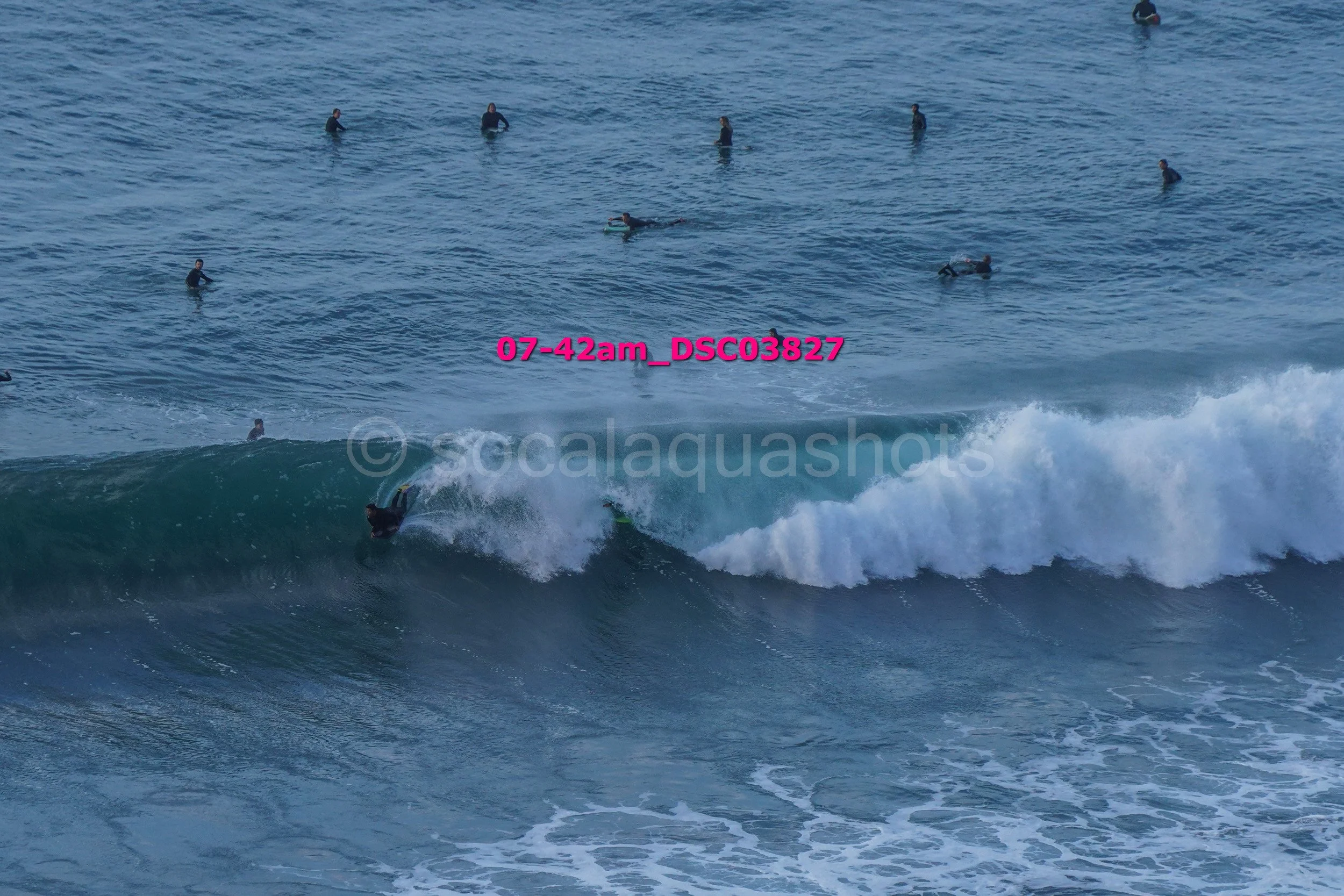 Surfer riding a wave at the beach with multiple people in the water watching.