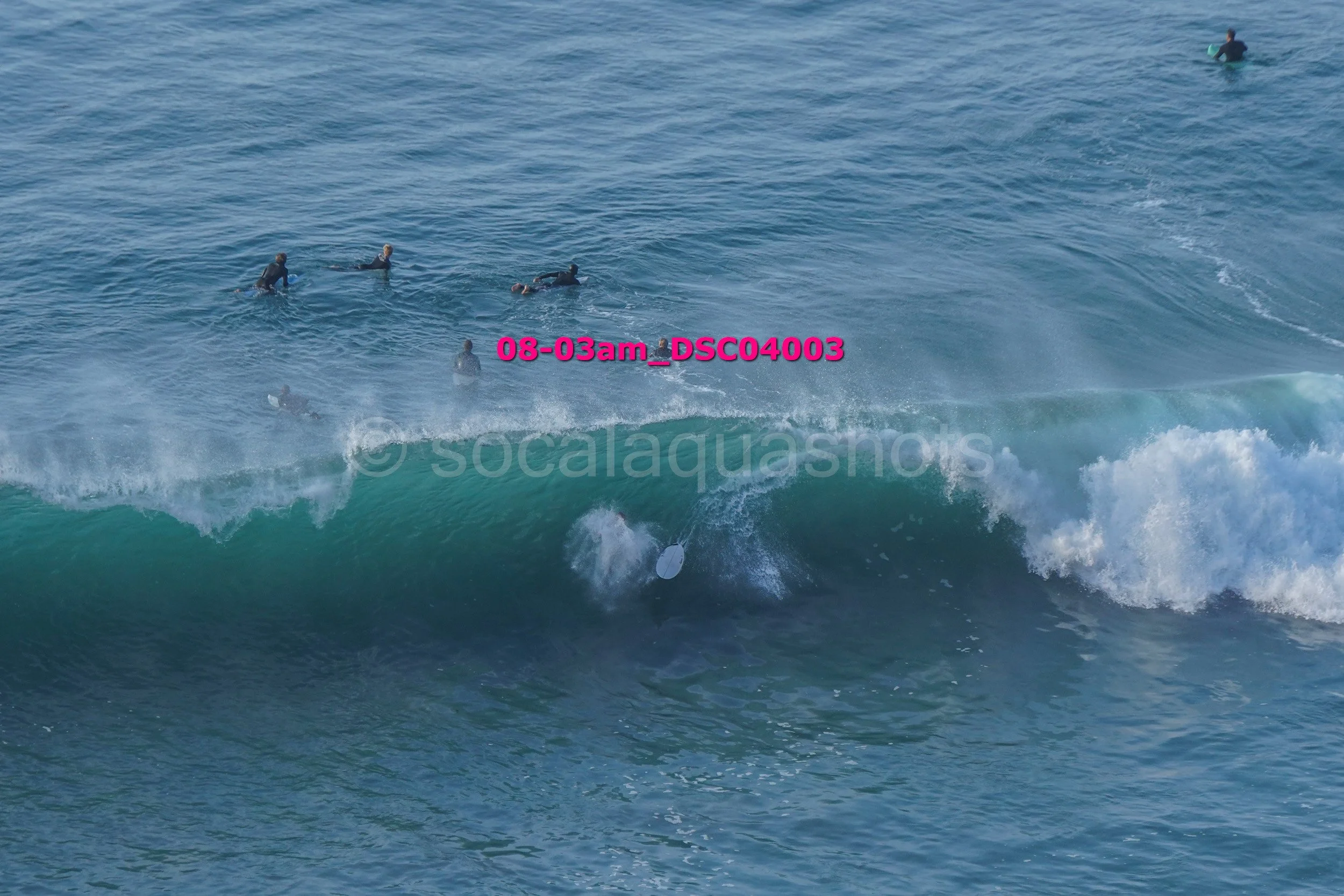 Surfers in the ocean waiting for or riding a wave with a surfboard submerged under the water.