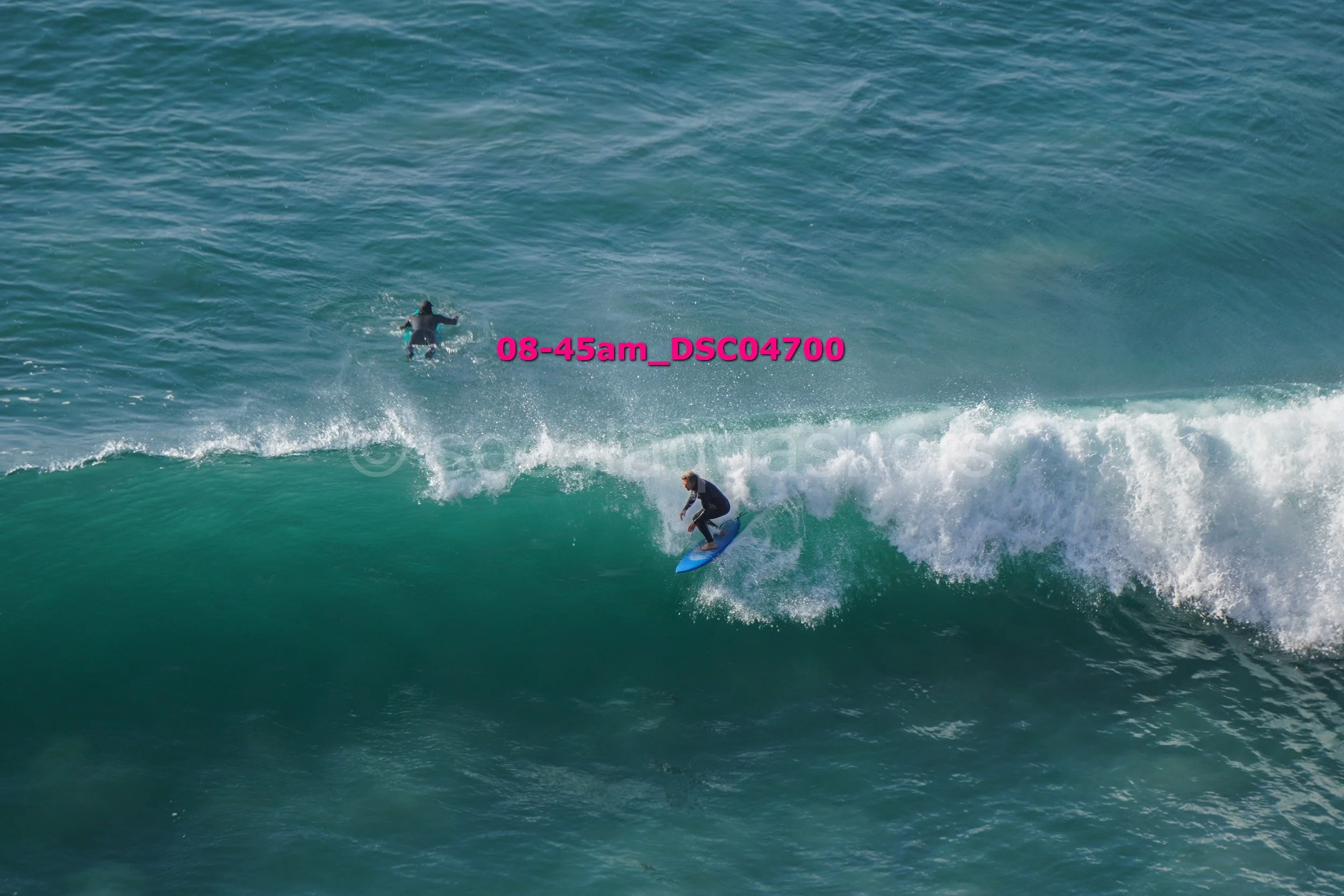 A person surfing on a wave in the ocean with another person swimming in the background.