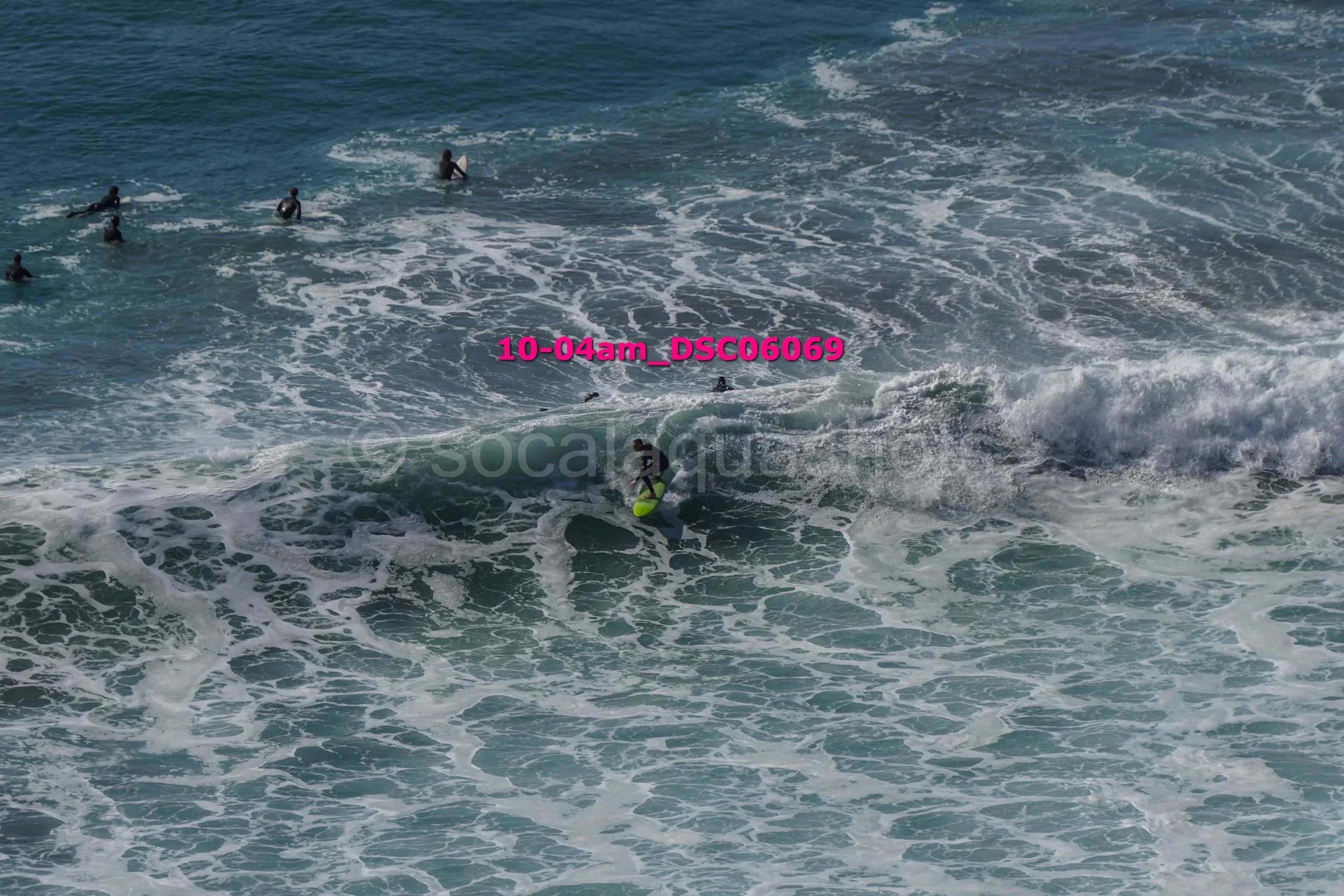 Surfer riding a wave in the ocean with several people swimming nearby
