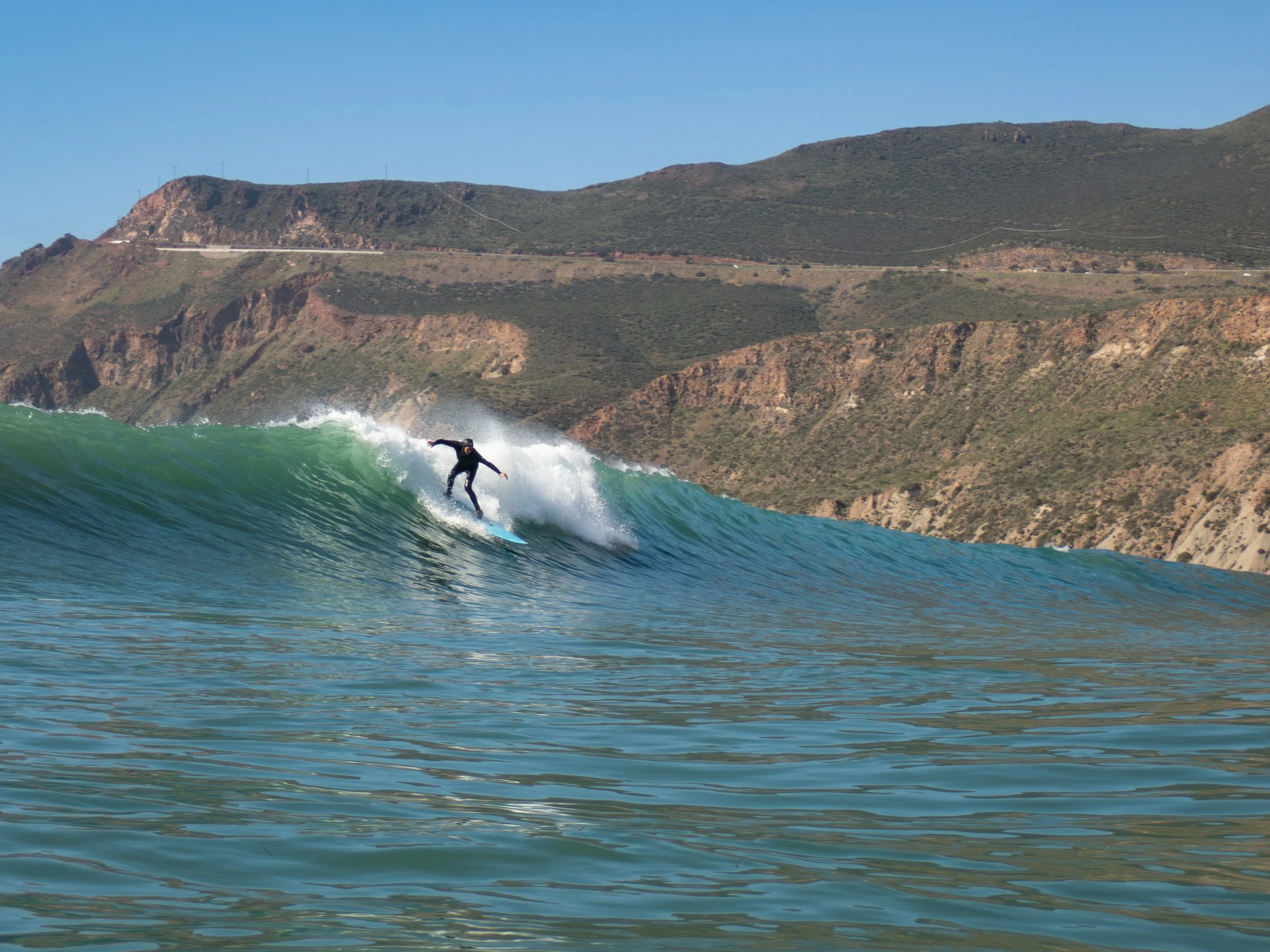 A person surfing on a wave with a mountainous landscape in the background.