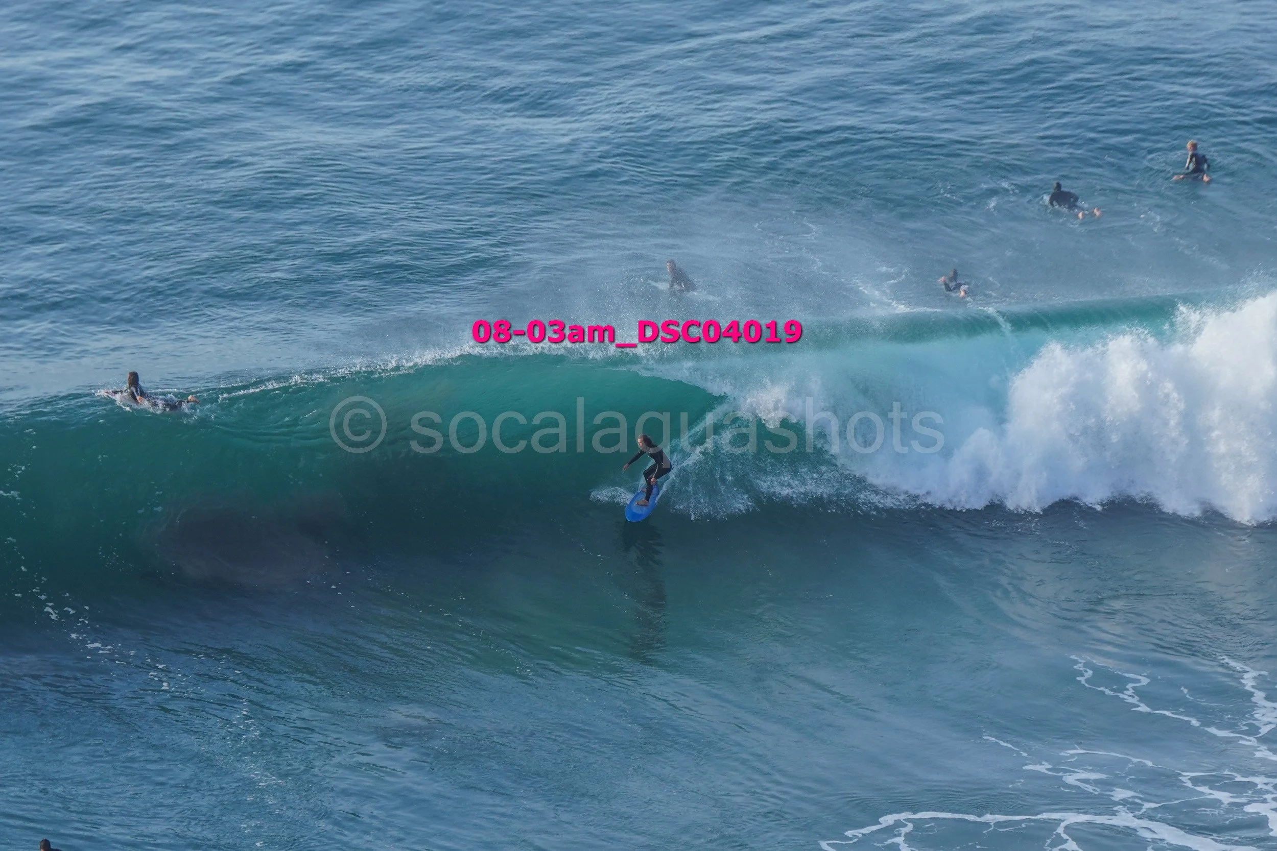 A surfer riding a large wave while several surfers are in the water, some paddling on their surfboards and others sitting on their boards in the ocean.