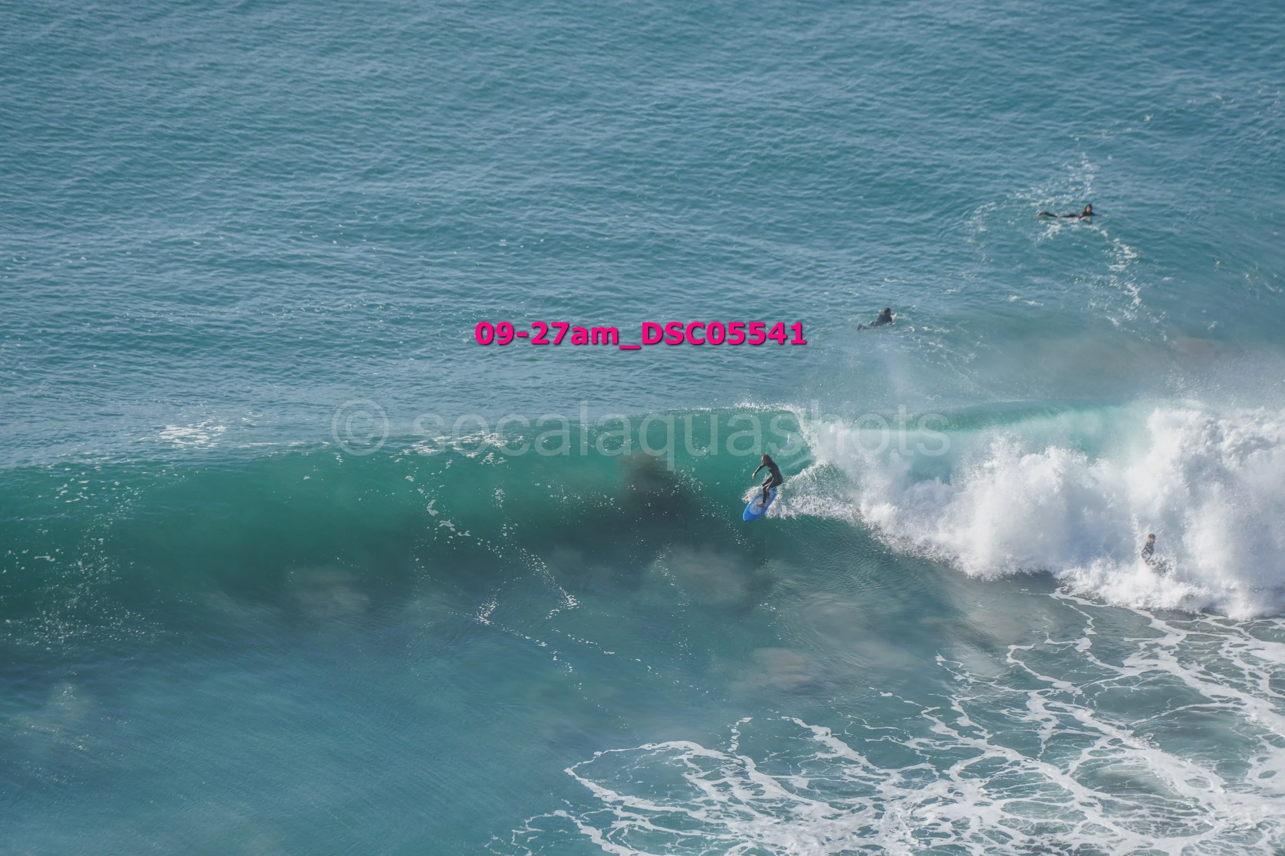 Surfer riding a large wave with three other surfers in the ocean nearby.