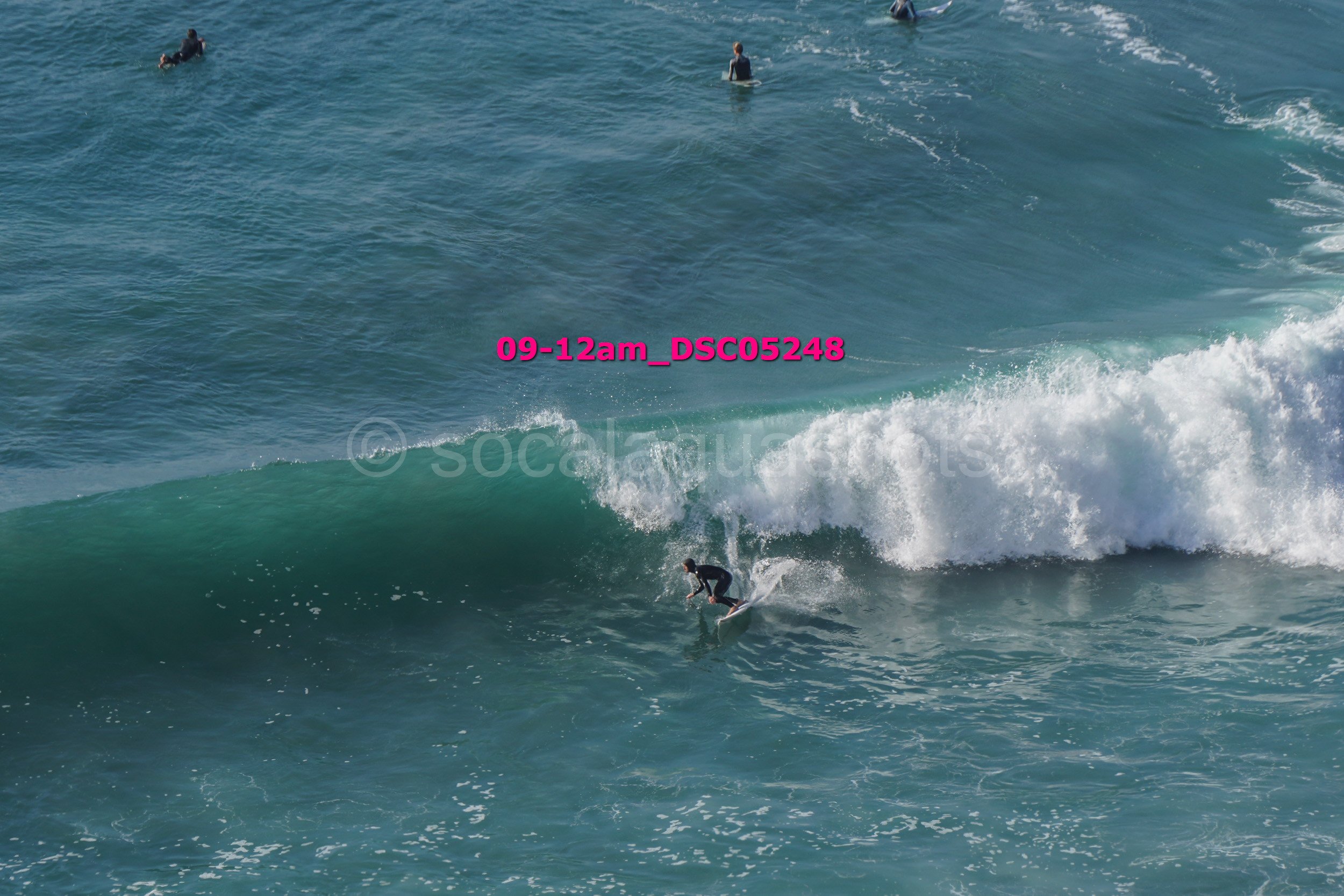 Surfer riding a wave in the ocean with several people in the background