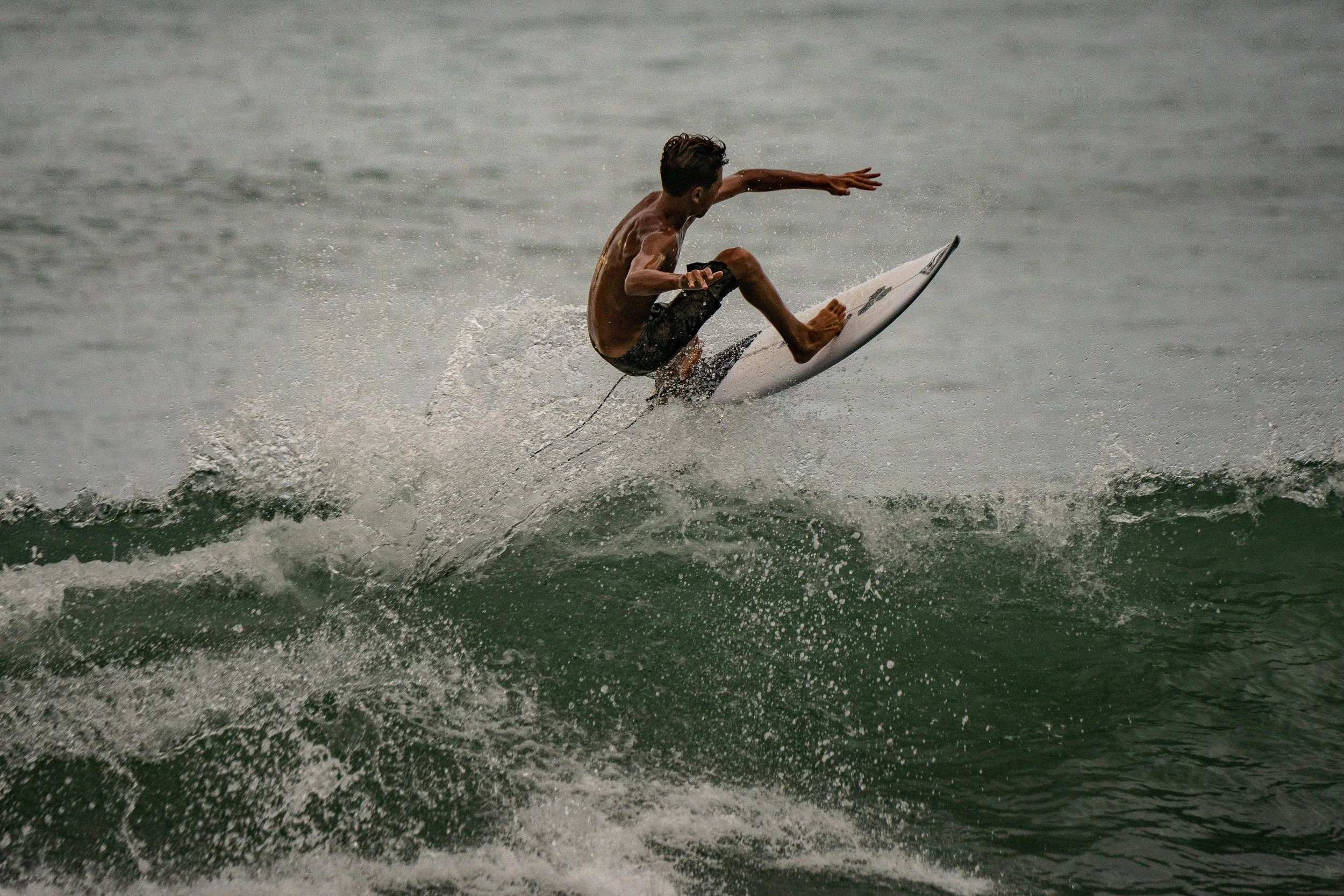 A young man surfing on a wave in the ocean, wearing black swim trunks and riding a white surfboard.