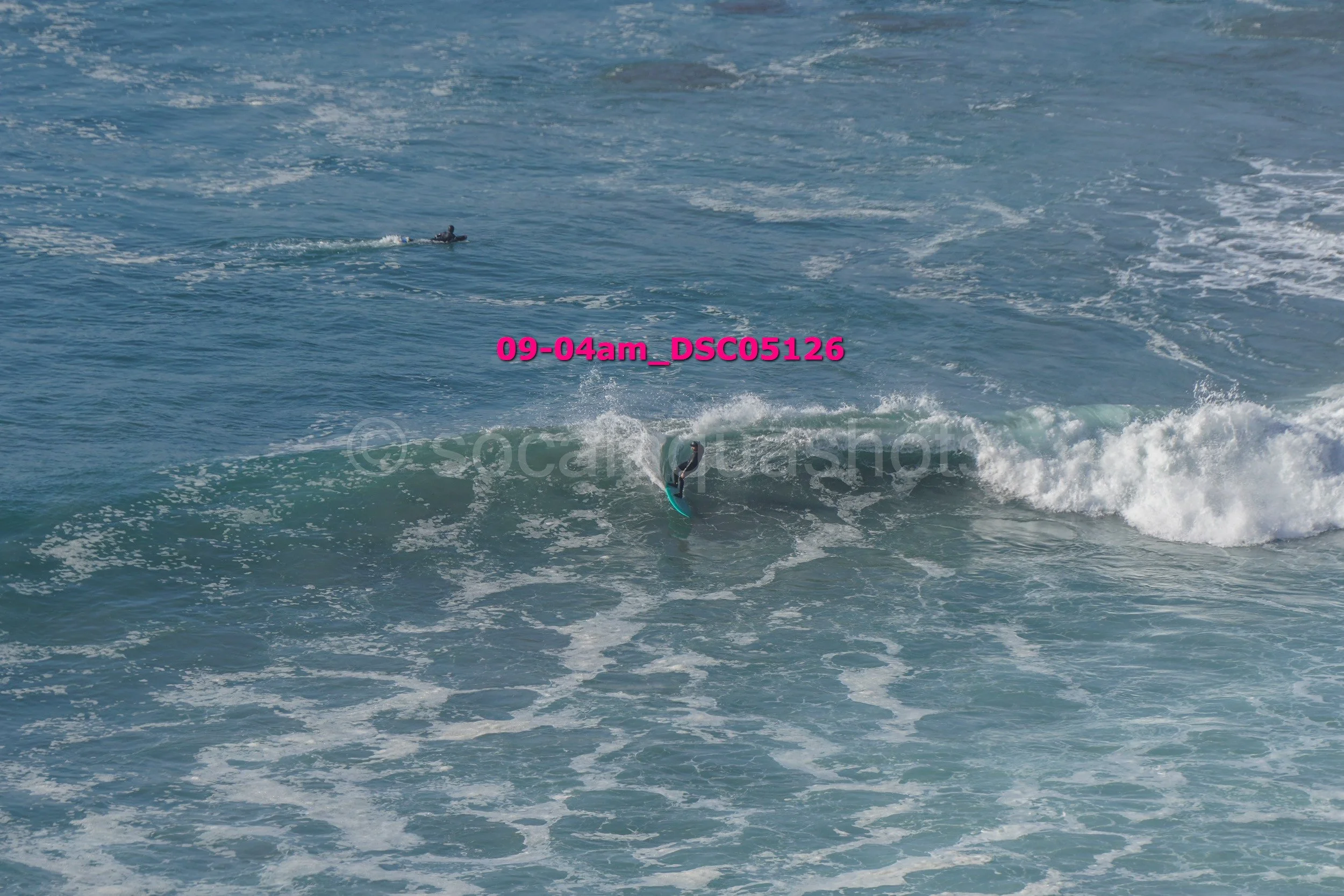A person falling off a surfboard in the ocean, with a boat in the distance, and ocean waves.