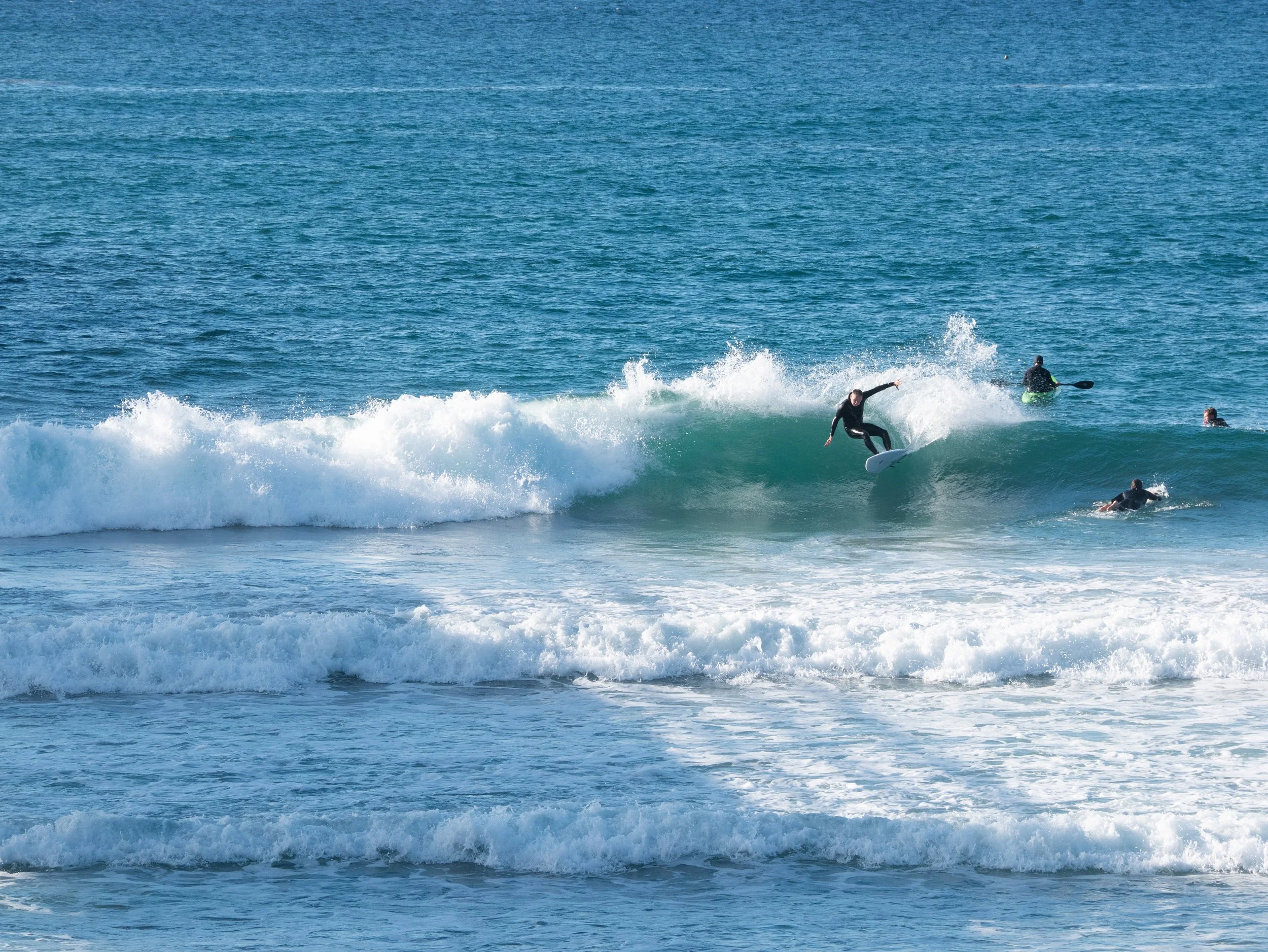 Surfer riding a wave at the beach with other surfers and paddleboarders in the background.