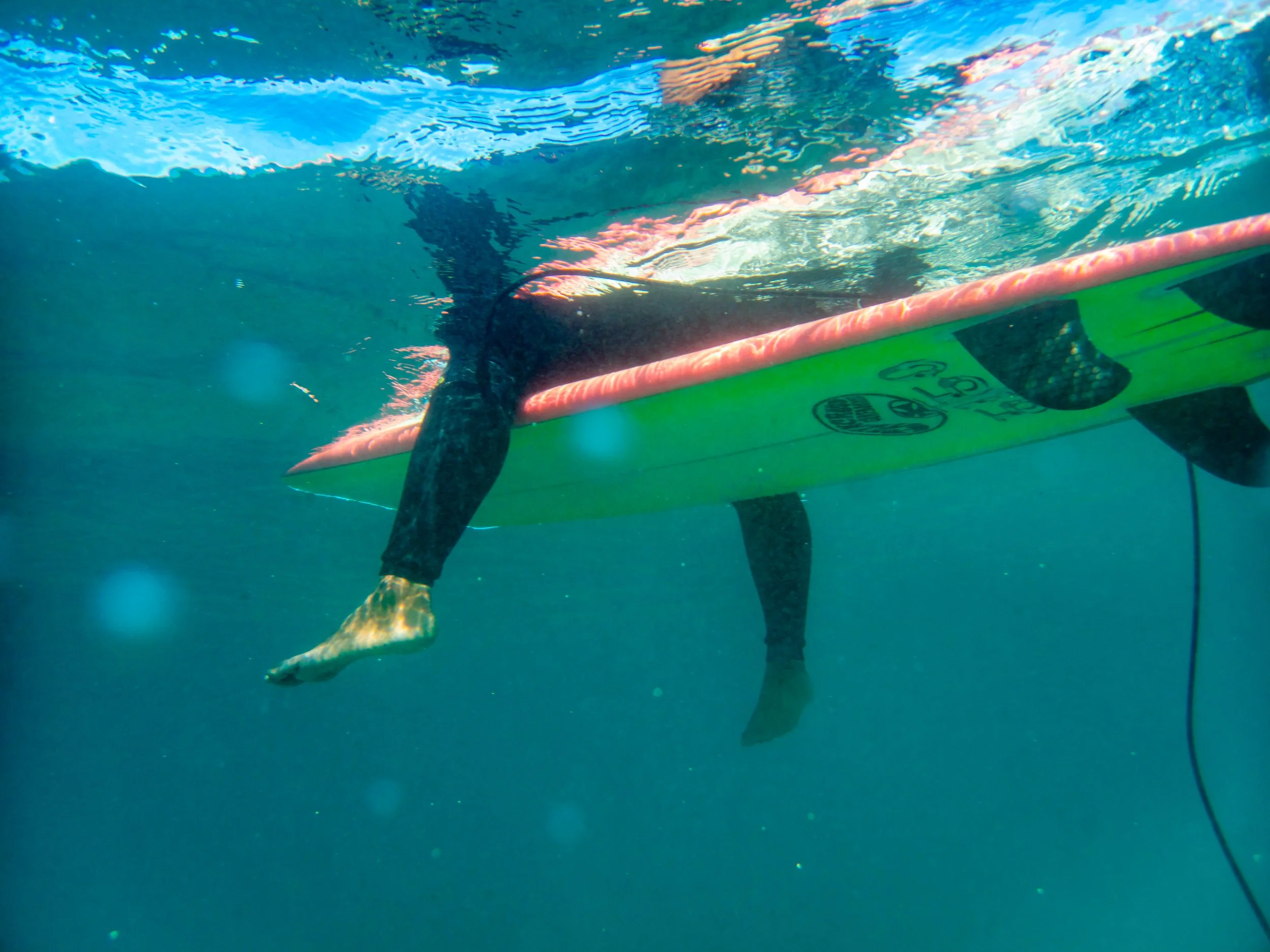 Person in wetsuit paddleboarding on a surfboard underwater, with only legs and feet visible.