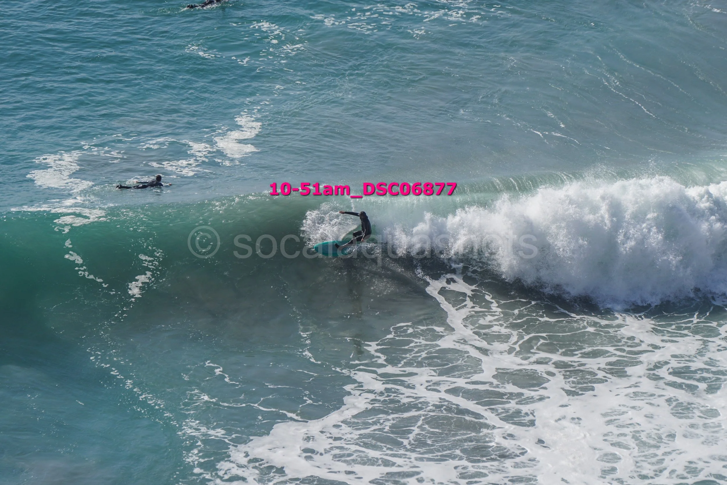 Surfer riding a wave while another person paddles in the ocean nearby.