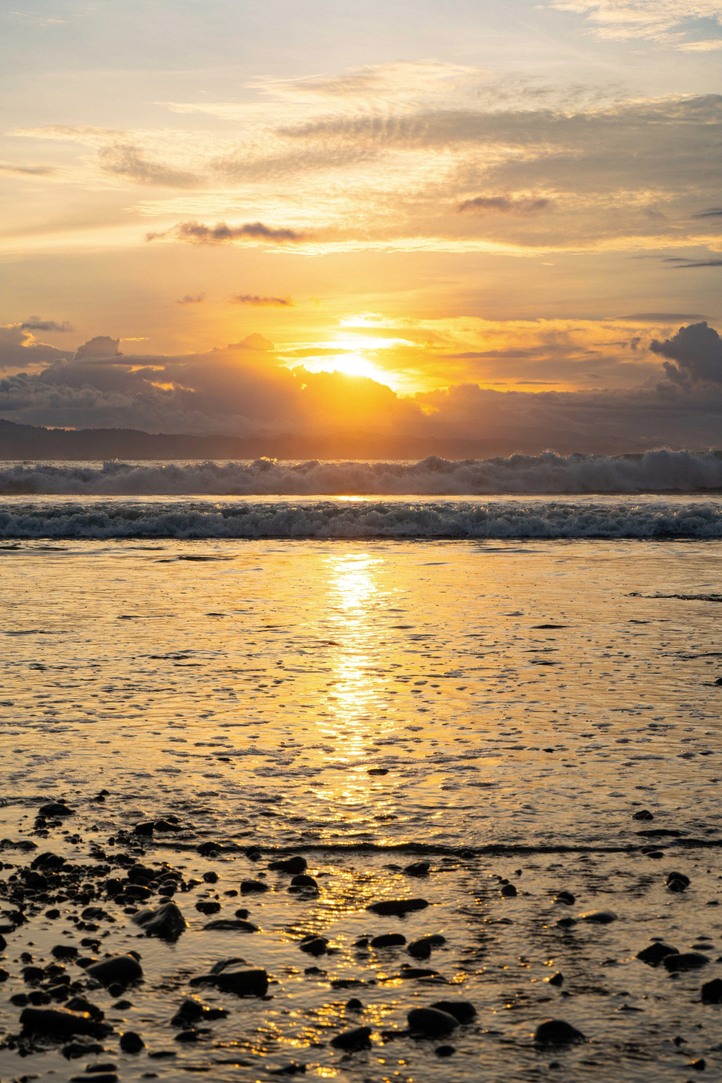 Sunset over the ocean with clouds in the sky and rocks in the foreground.
