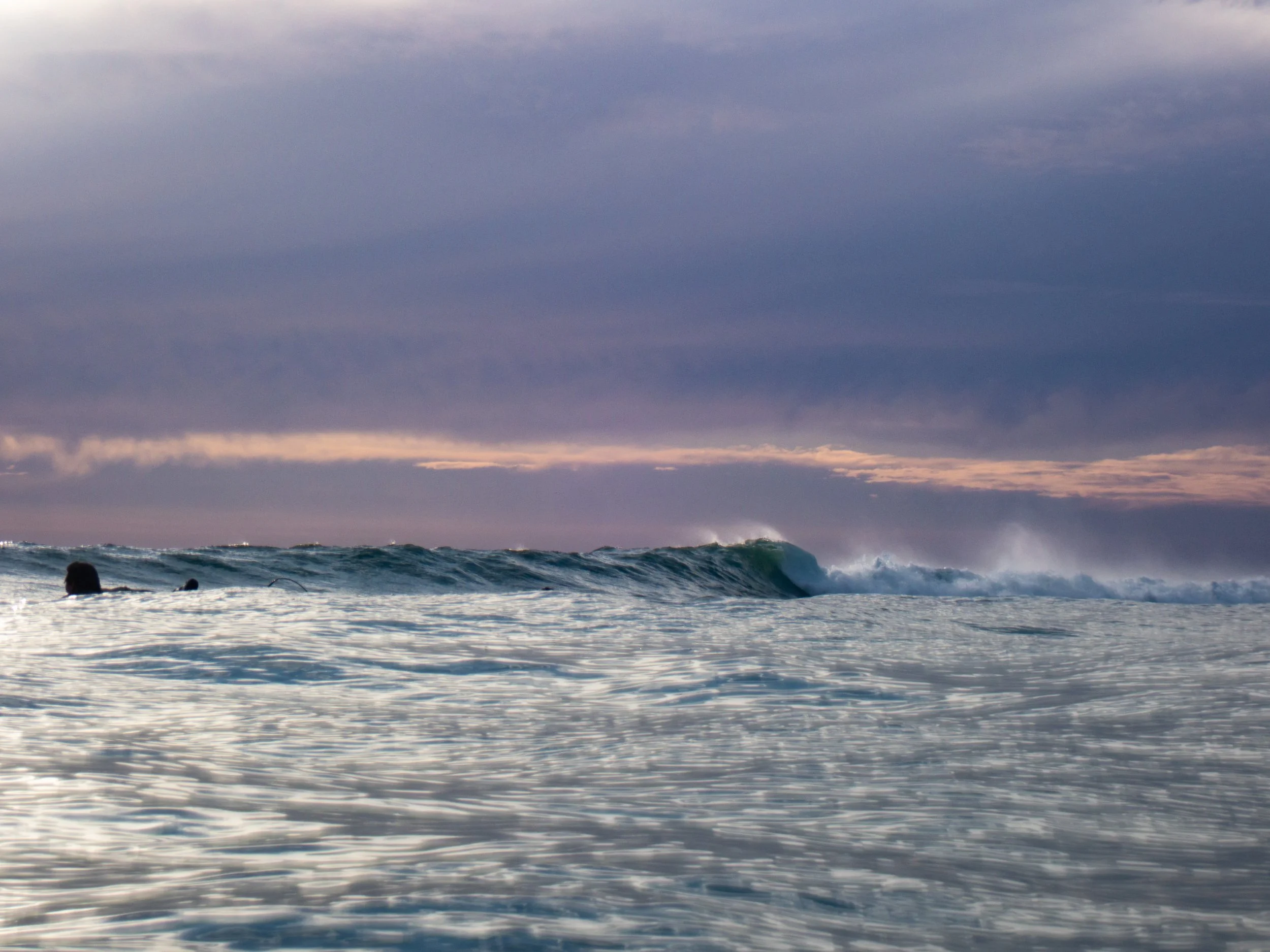 Surf surfers in the ocean with waves under a cloudy sky.