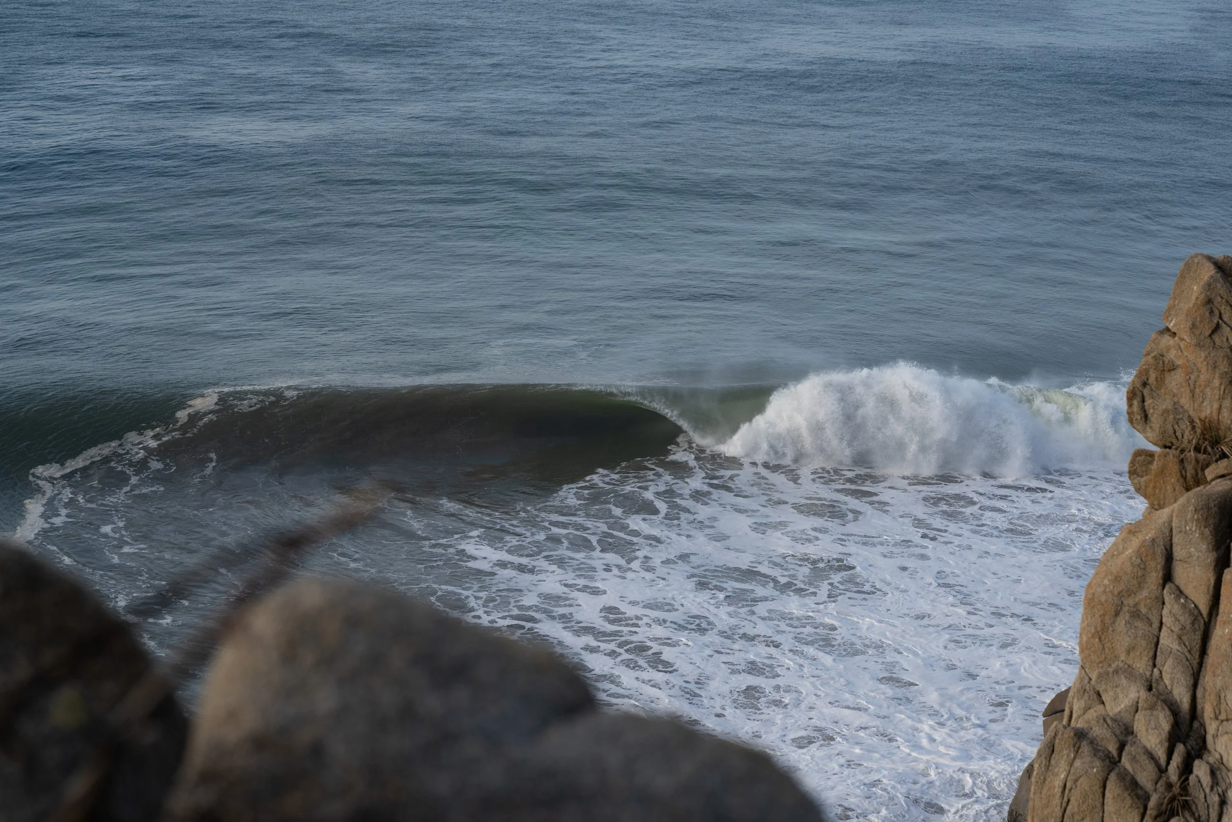 Ocean waves crashing against rocks, viewed through gaps in a rocky coastal area.