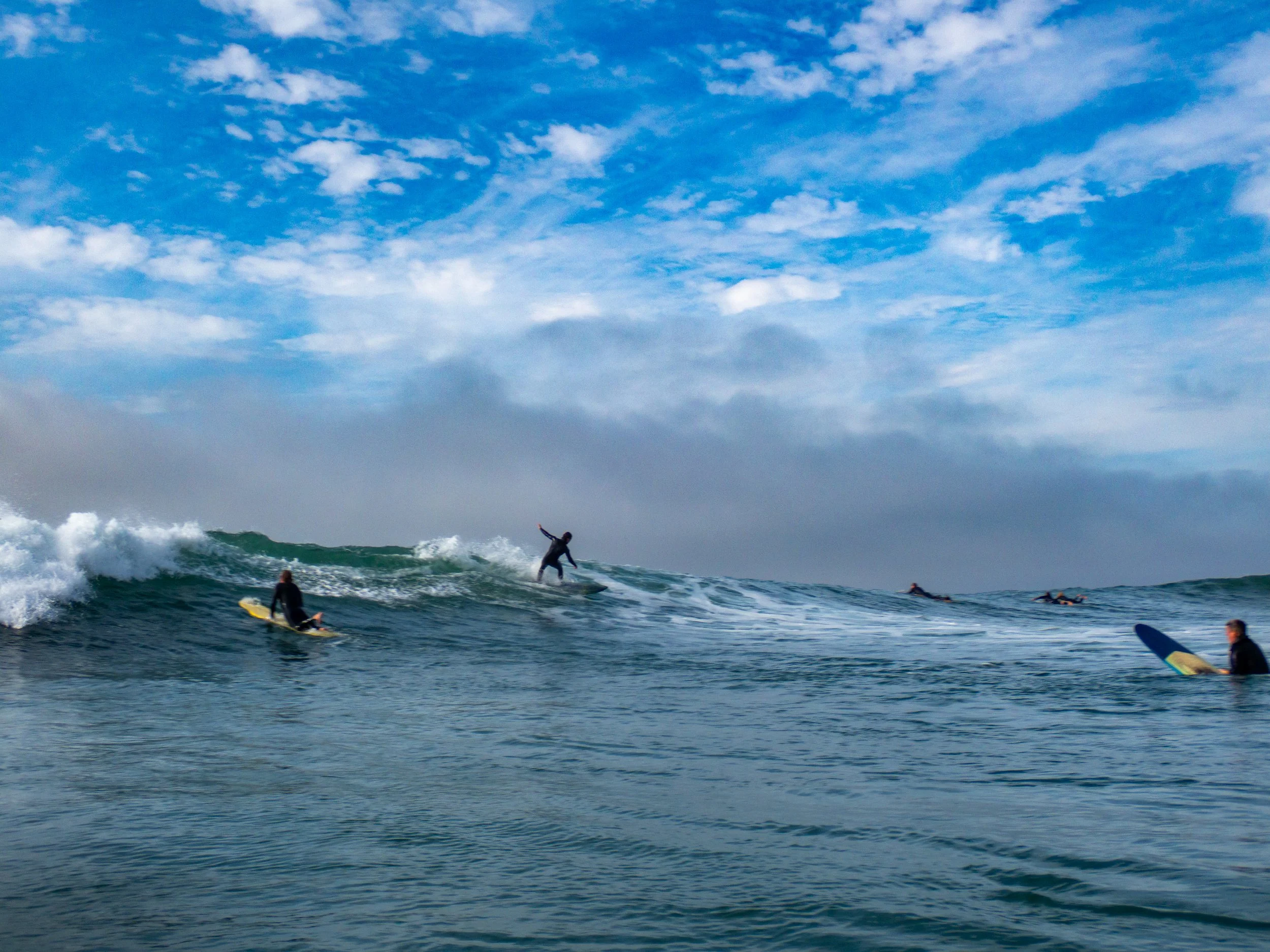 Surfers riding waves in the ocean under a partly cloudy sky.