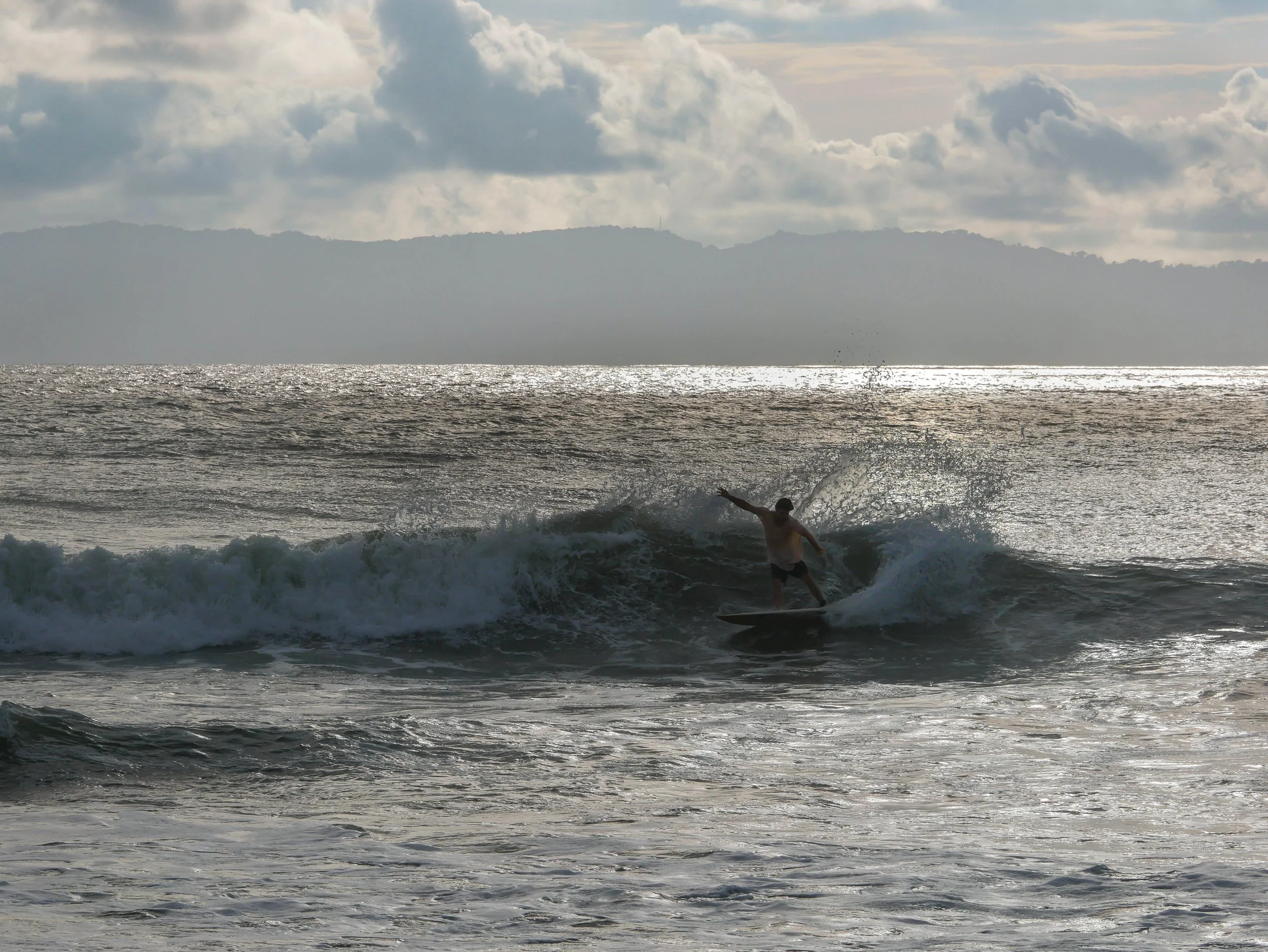 Surfer riding a wave at sunset on the ocean with a cloudy sky.