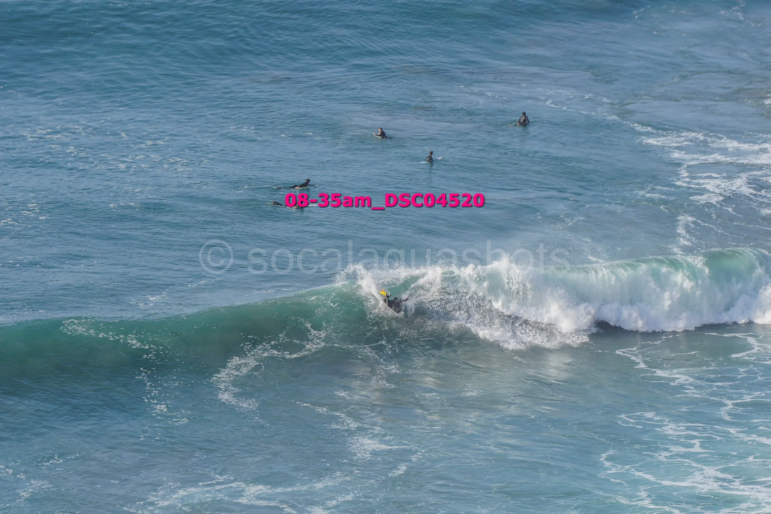 Surfer riding a wave with several people swimming in the ocean in the background.