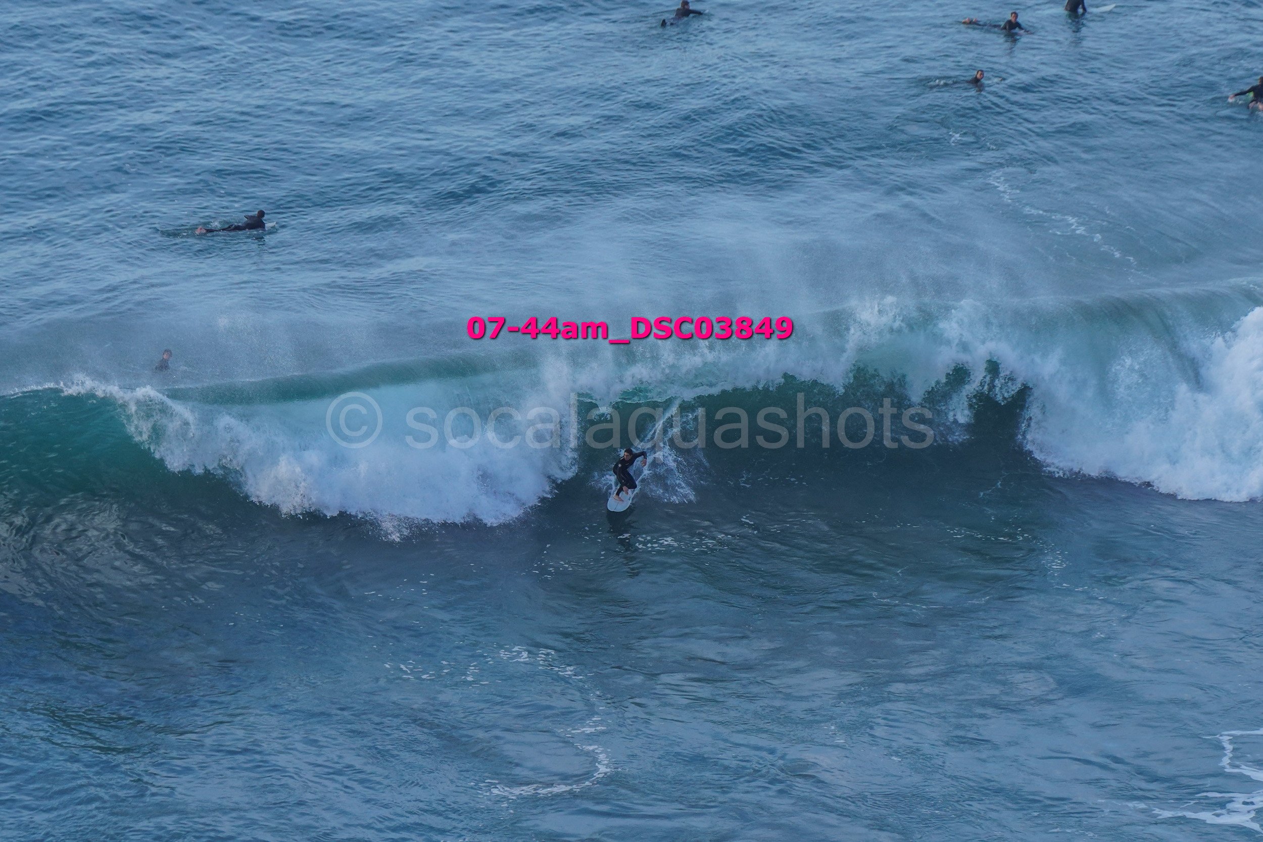Surfer riding a wave with several other surfers in the water around him.