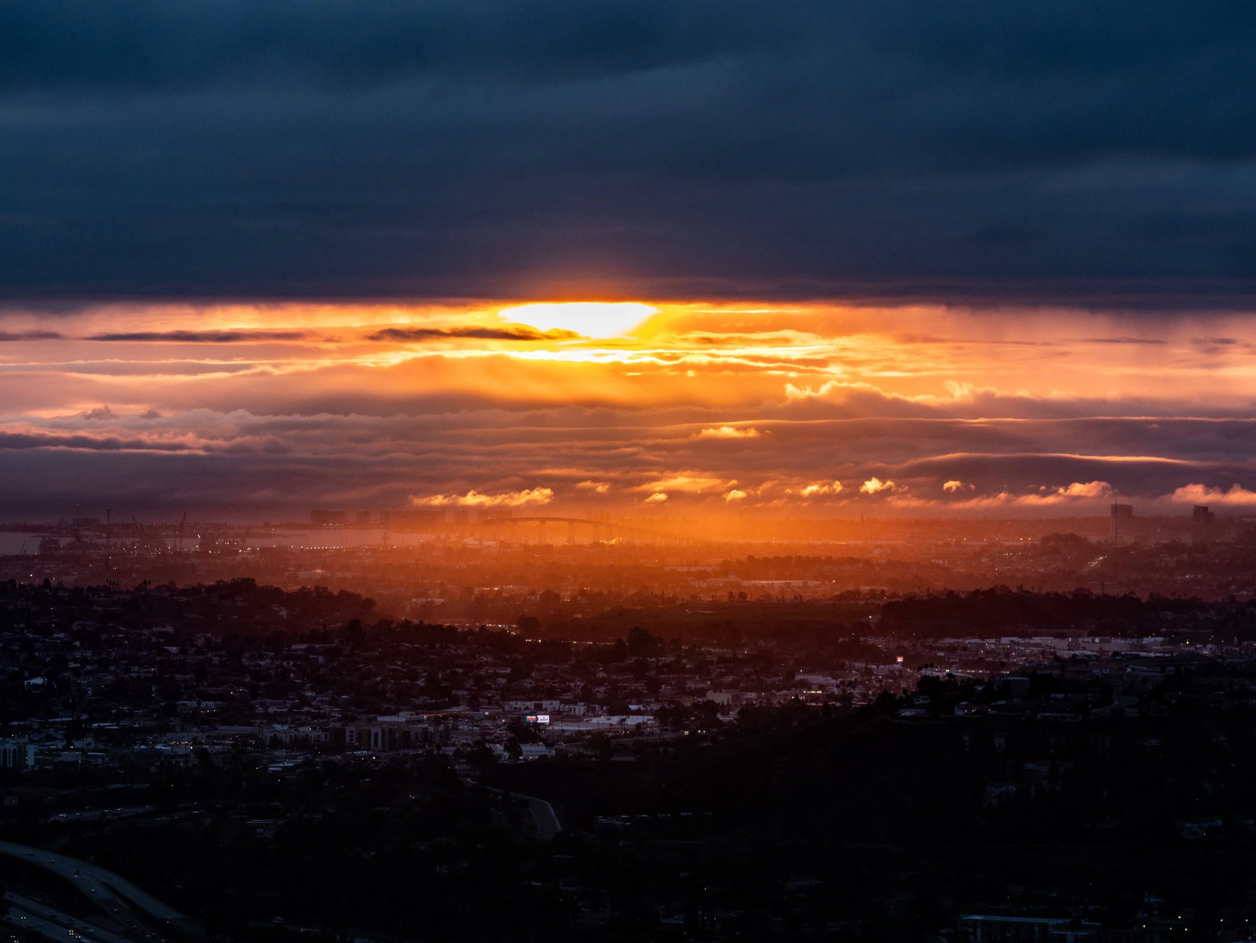 Sunset over a city with dark clouds in the sky, casting an orange glow on the horizon and cityscape below.