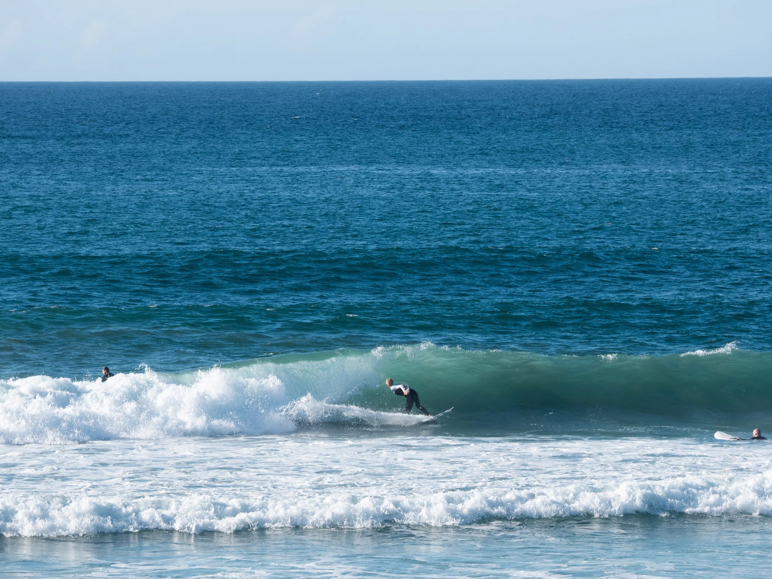 A person surfing on a wave in the ocean with two other surfers visible in the water.