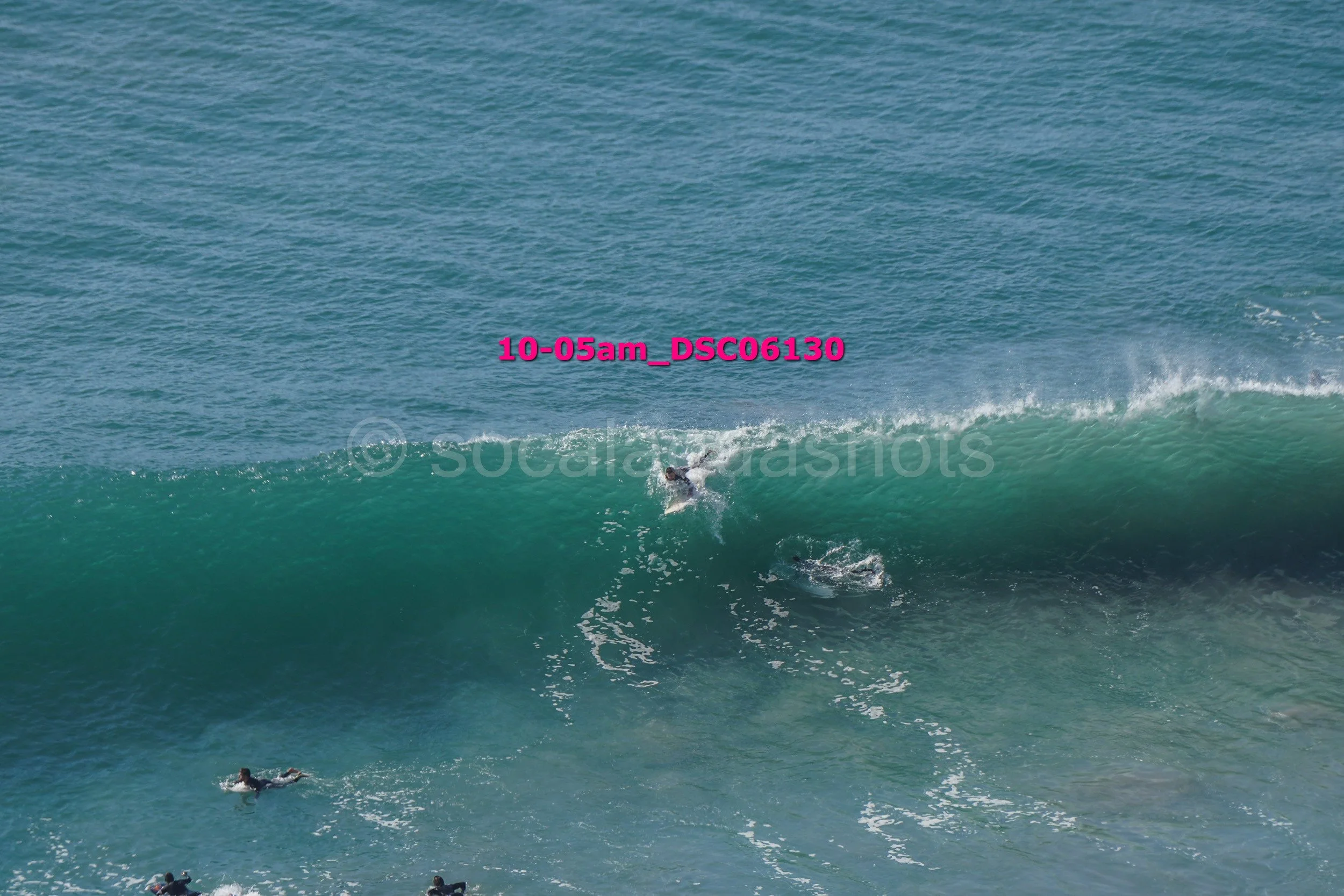 Surfer riding a wave in the ocean, with several other surfers waiting in the water.