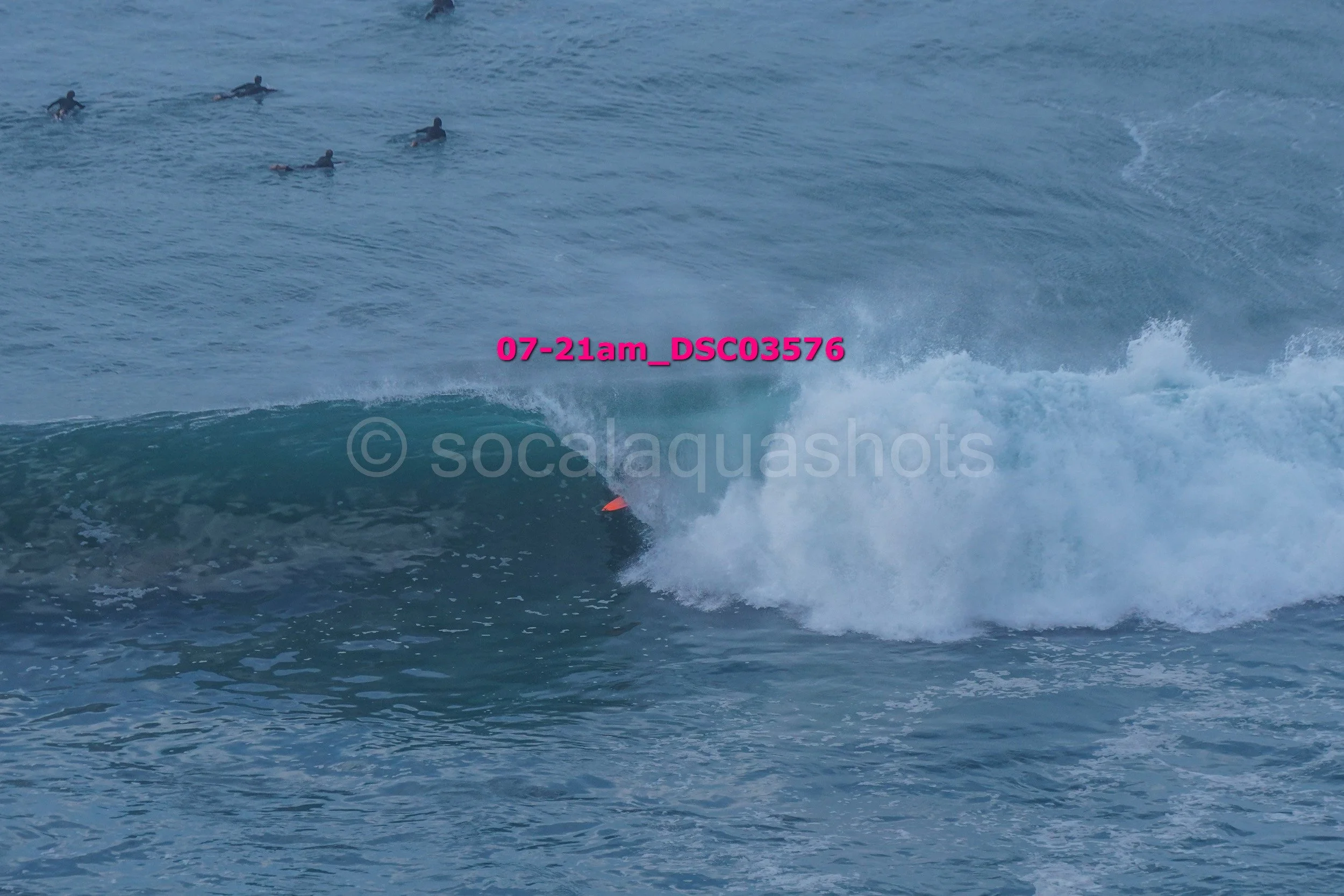 Surfer riding a wave in the ocean with several people swimming in the background.