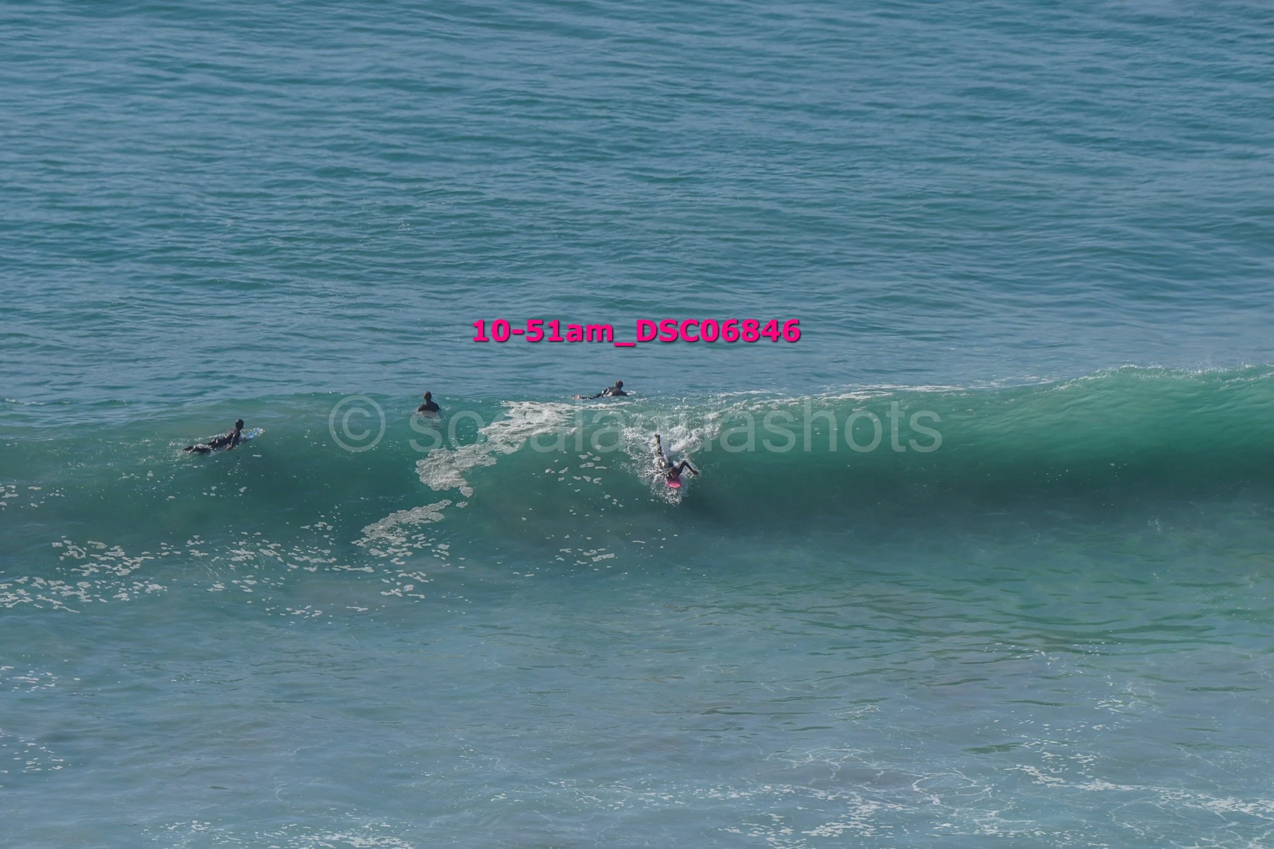People surfing in the ocean on a wave, with one person falling off their surfboard.