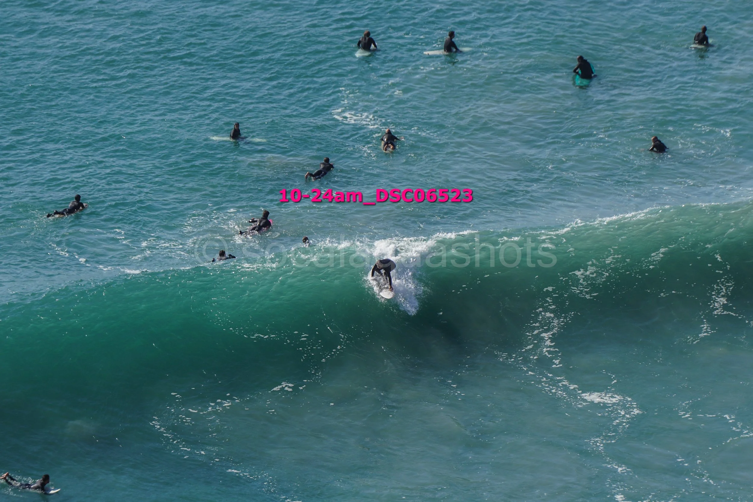 A group of surfers in wetsuits riding and waiting for waves in the ocean, with one surfer actively riding a wave.