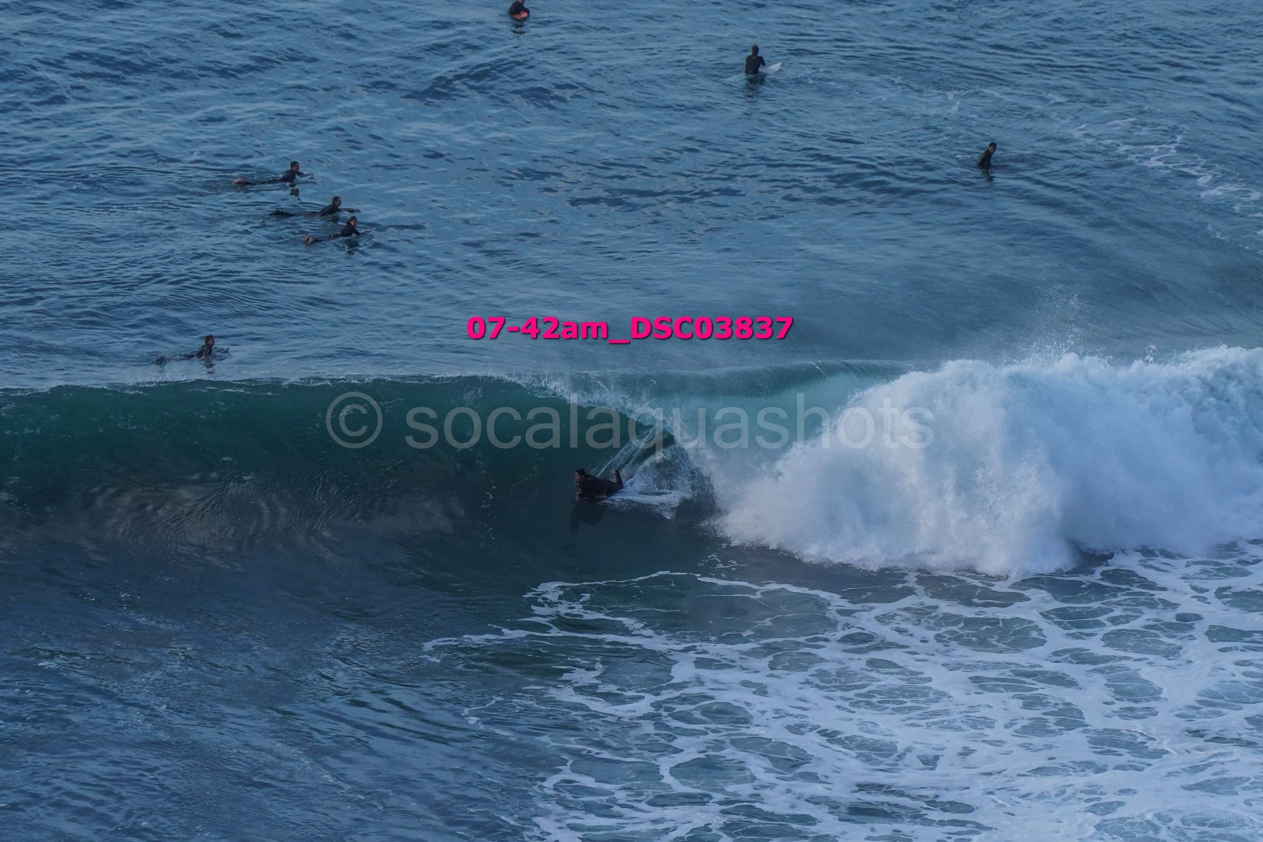 Surfer riding a wave while several people surf in the ocean in the background.