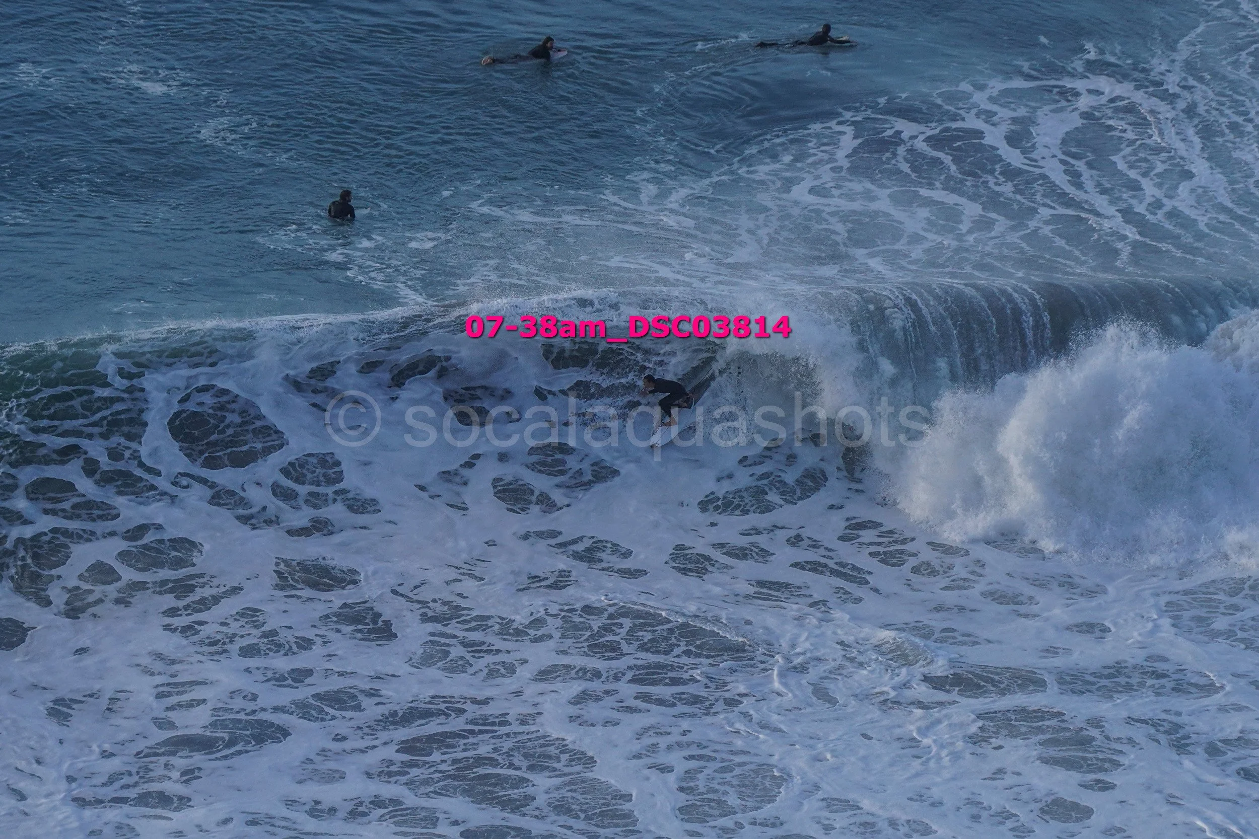 A person surfing on a wave in the ocean with several people swimming nearby.