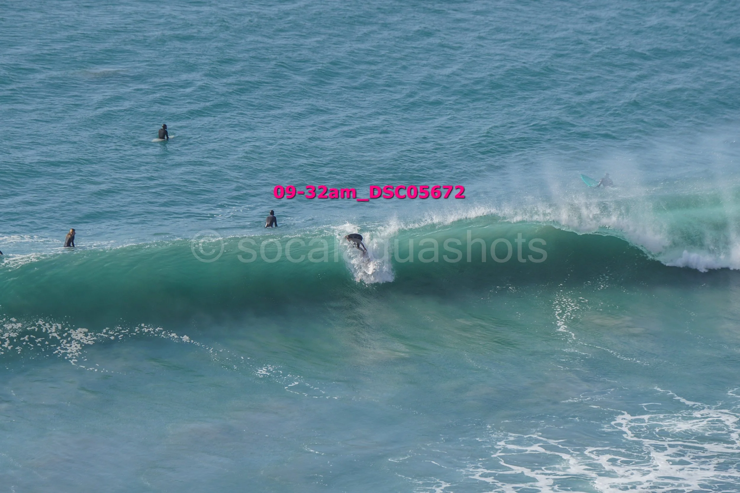Surfer riding a wave in the ocean with several other surfers watching or surfing in the background.