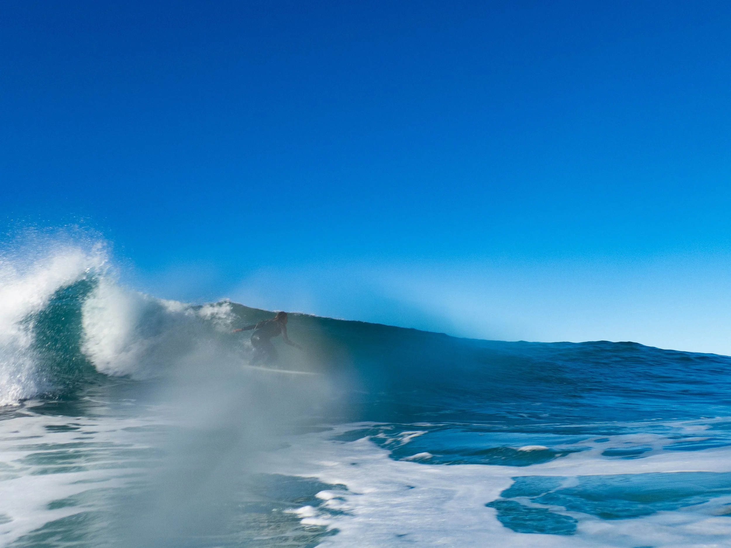 Surfer riding a wave in the ocean under a clear blue sky.