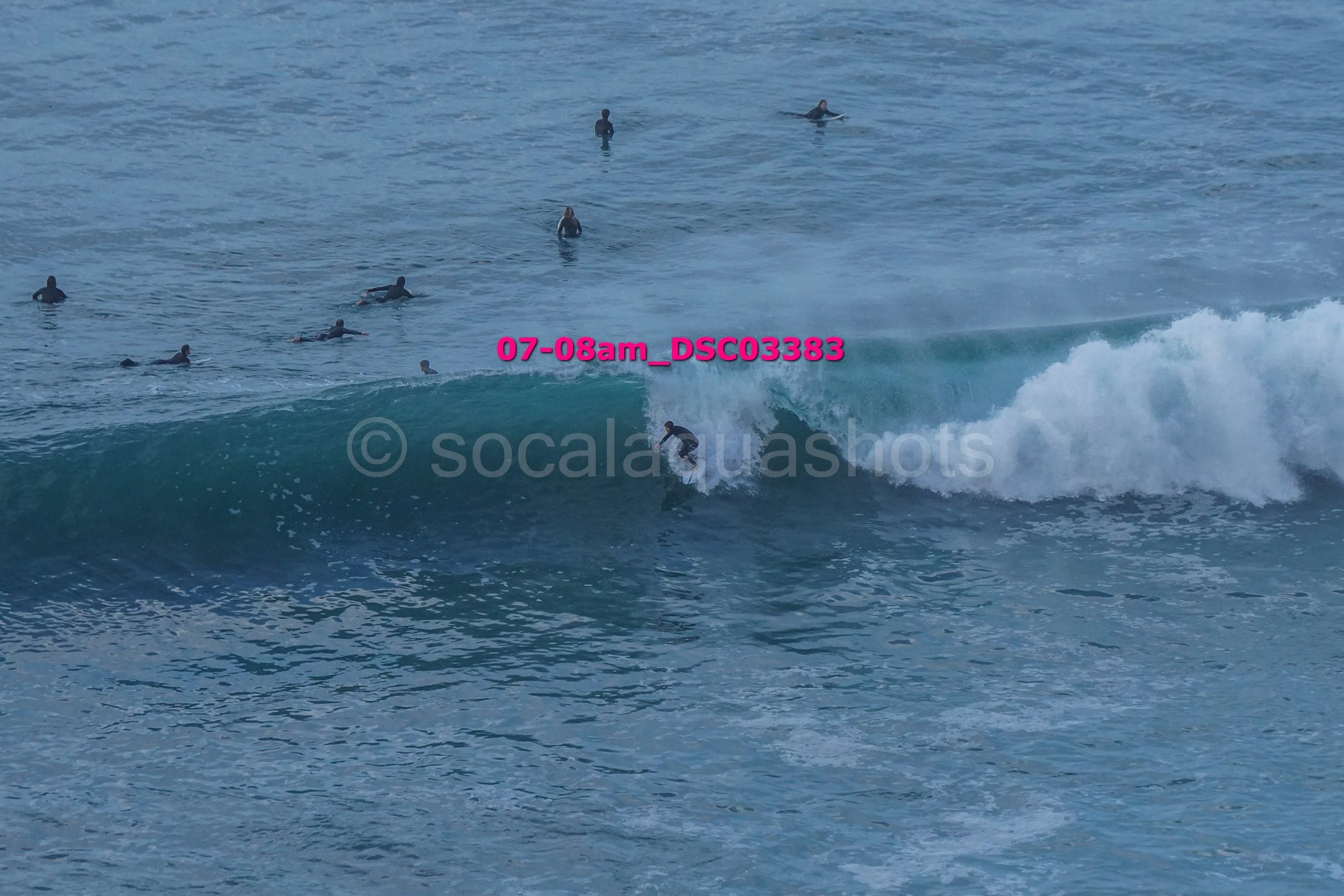 Surfer riding a wave with multiple surfers watching from the water