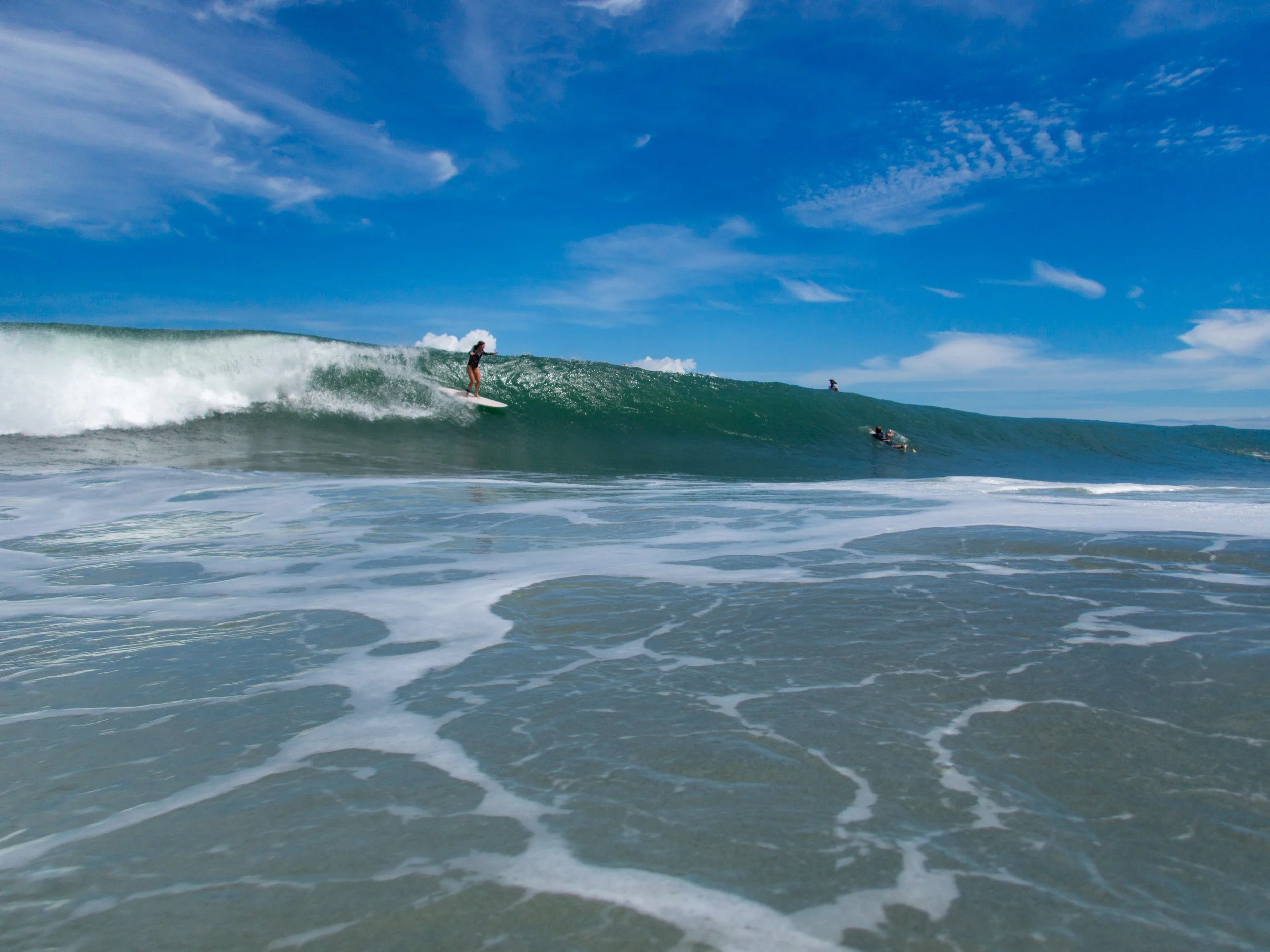 Surfer riding a wave in the ocean, with clear blue sky and foamy water.