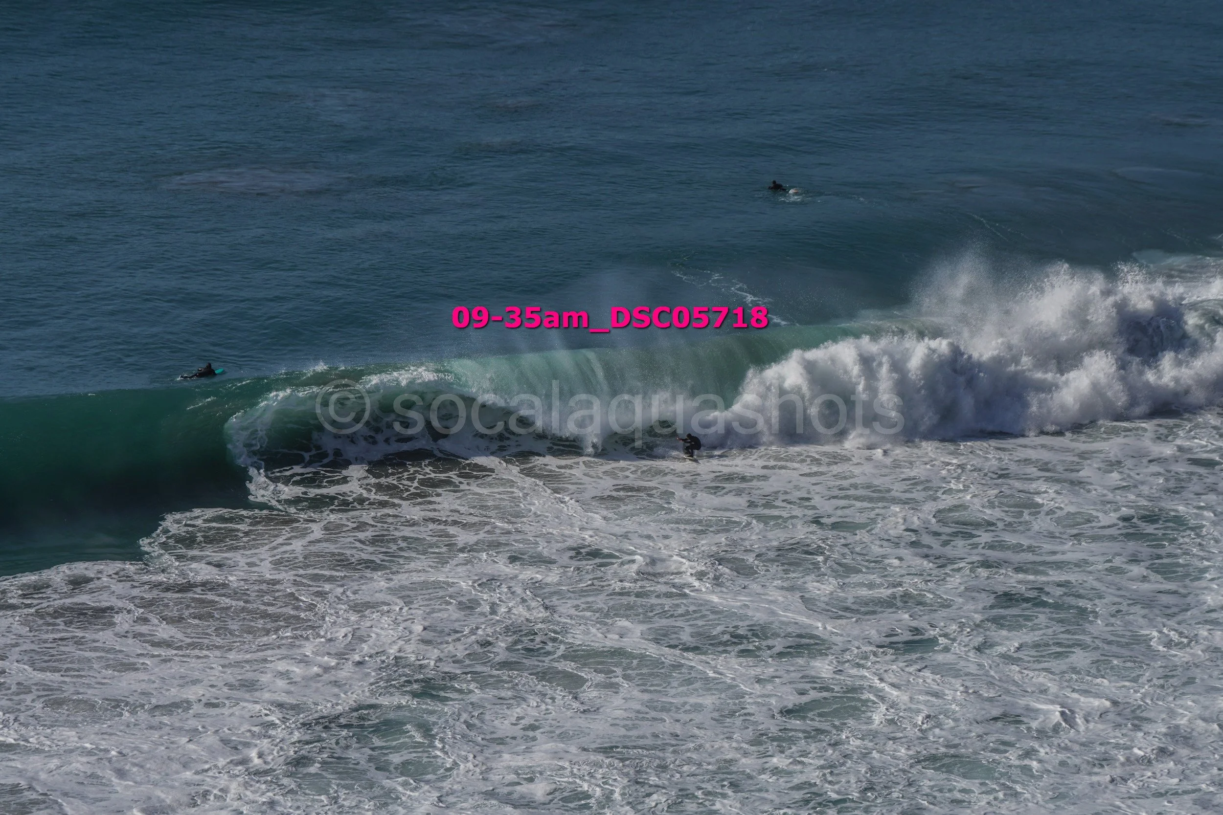 Surfers riding ocean waves during daytime with clear blue water.