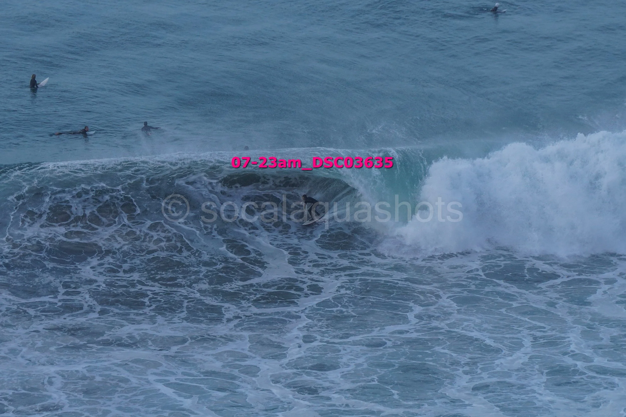 Surfer riding a wave with three other surfers in the distance in the ocean.