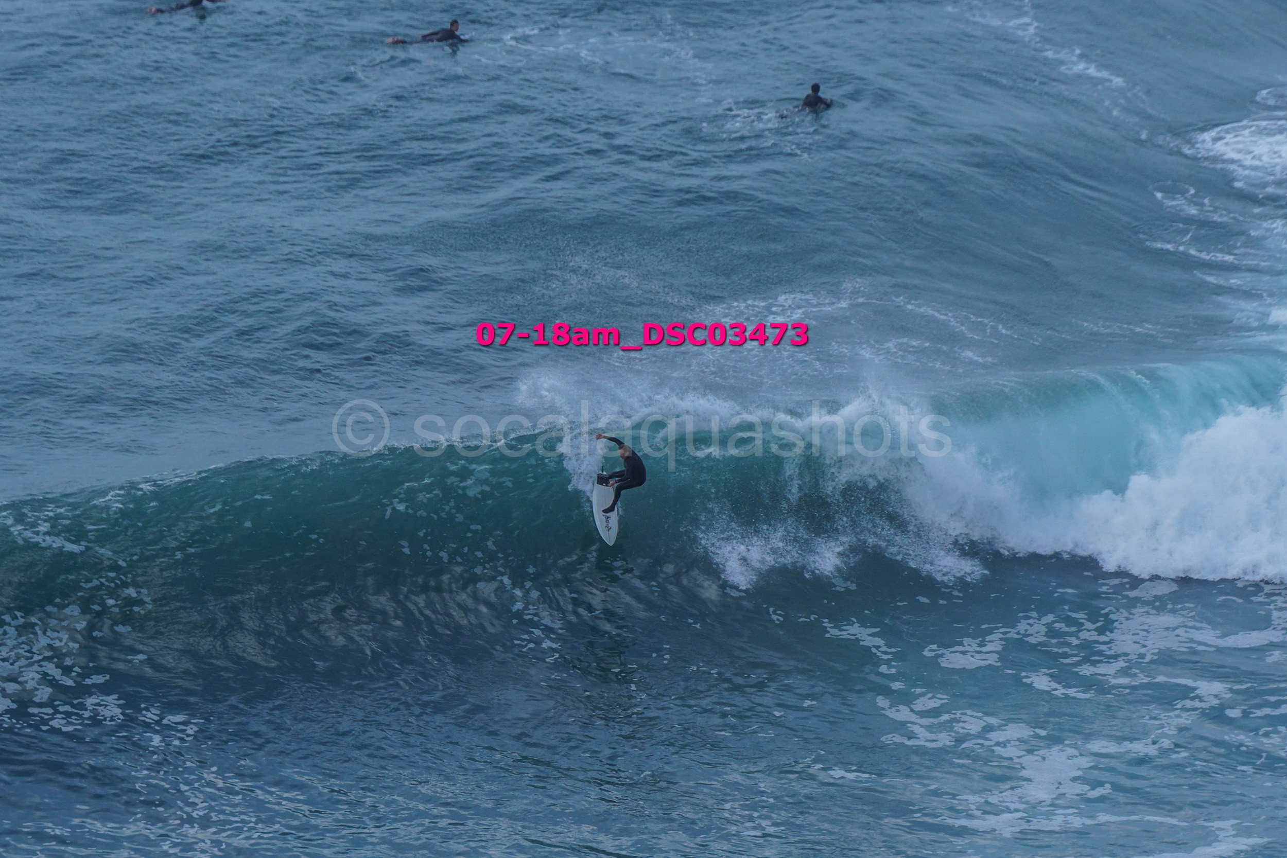 A person surfing on a wave in the ocean, with three other people in the water in the background.