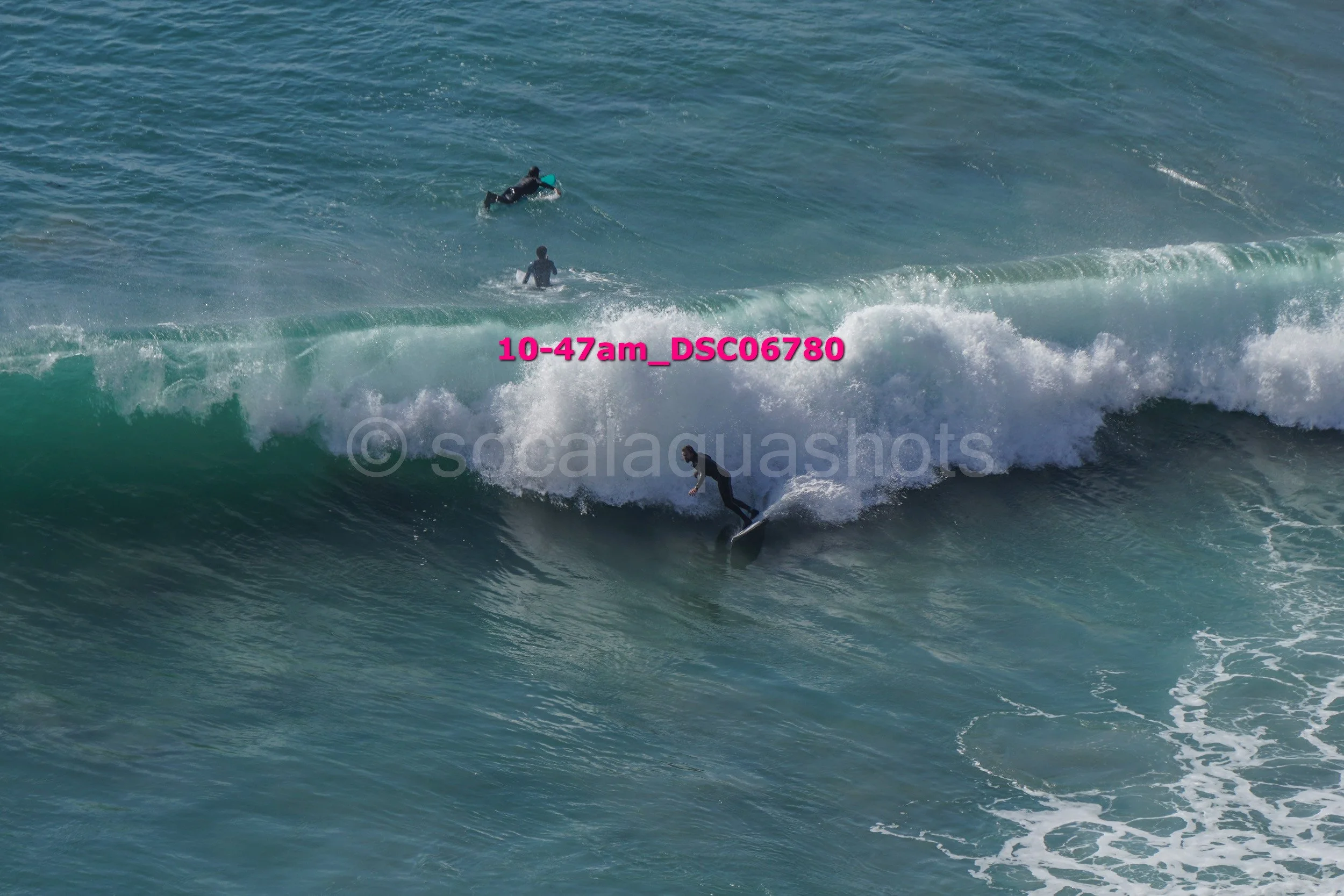A person surfing on a wave in the ocean with two other individuals swimming in the background.