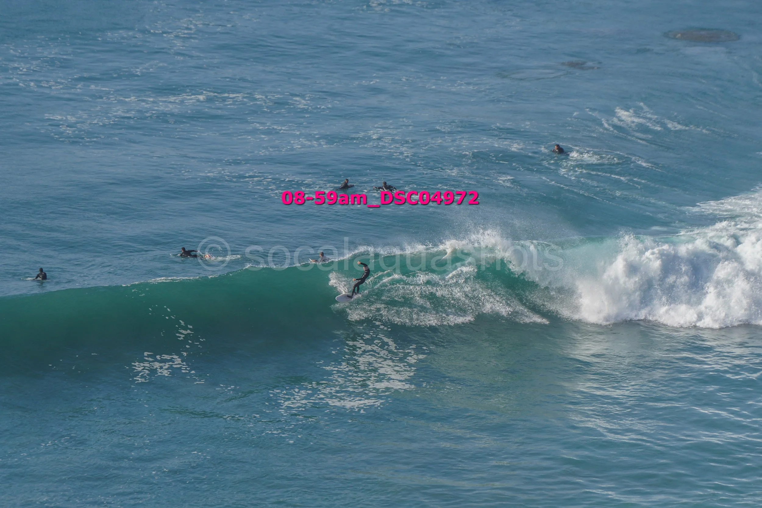 A surfer riding a wave with several other surfers in the water nearby.