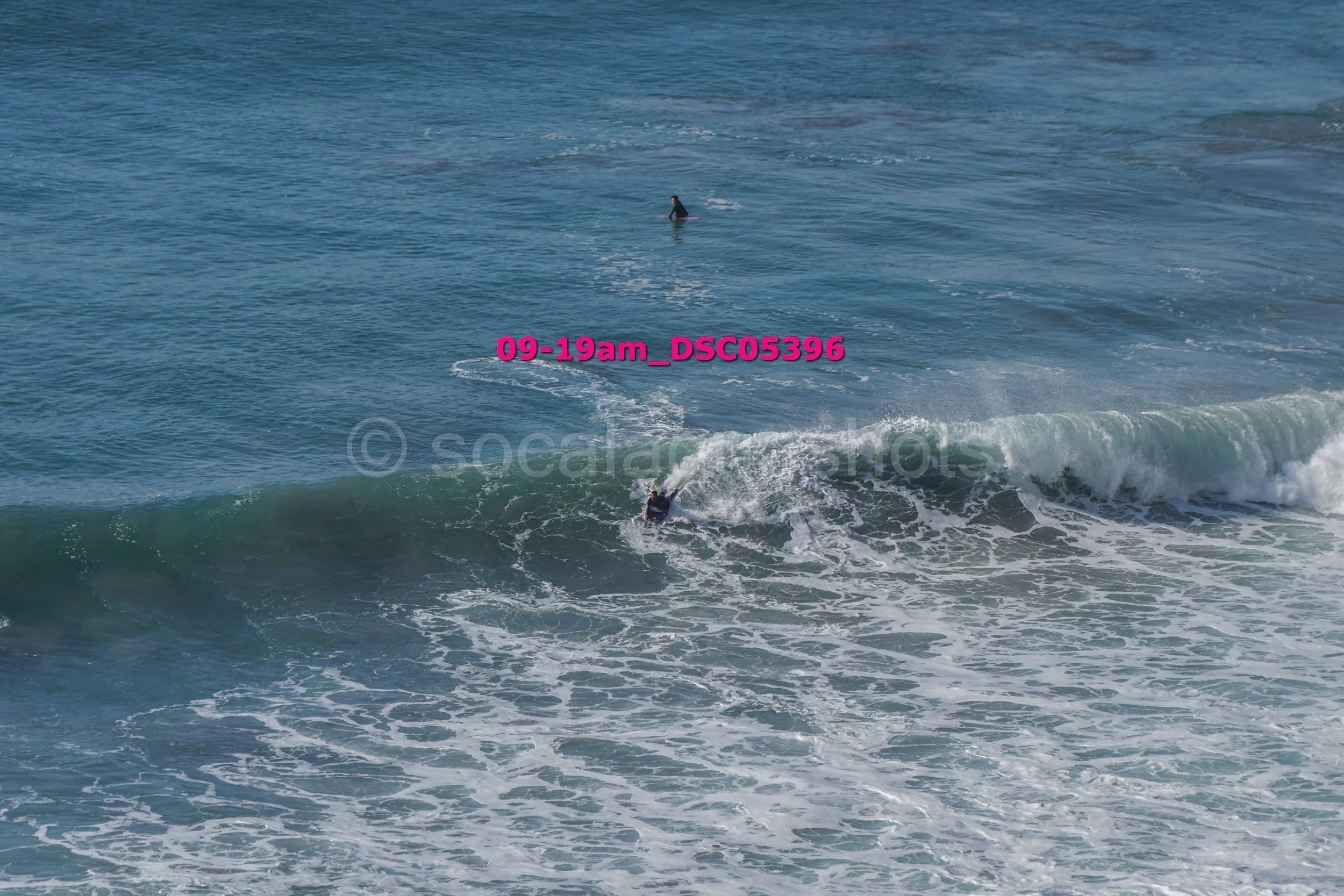 A person surfing in the ocean with another person swimming in the background.