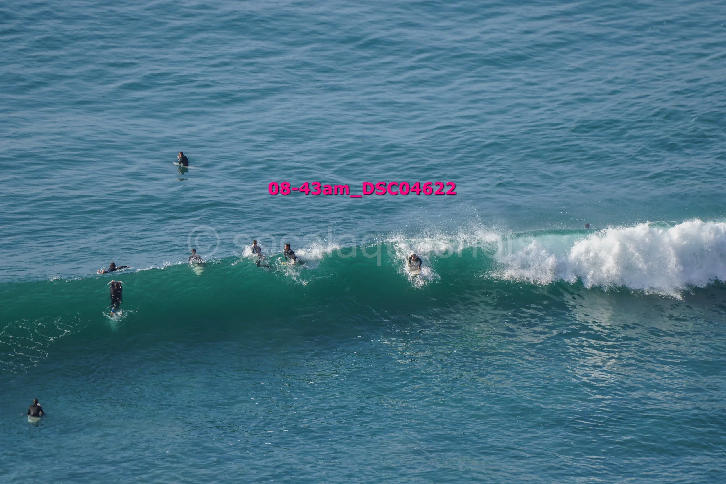 Group of surfers in wetsuits waiting and riding on ocean waves.
