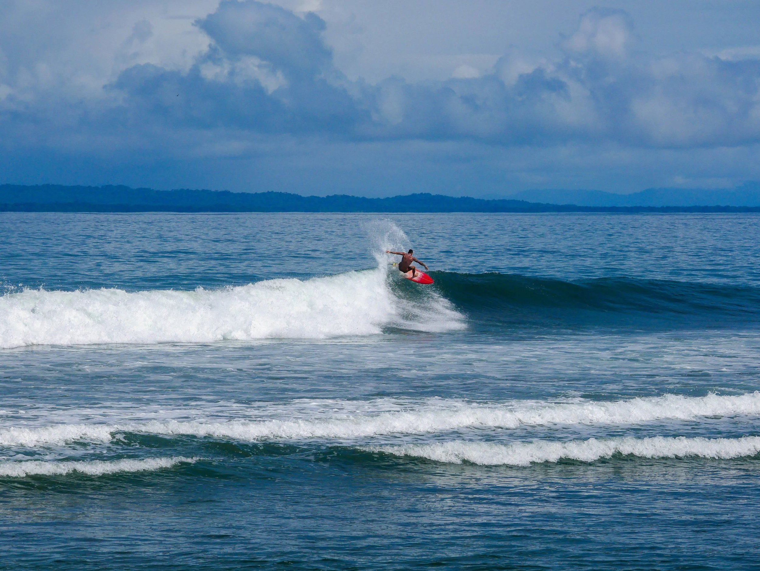 Surfer riding waves on a red surfboard in the ocean under a cloudy sky.
