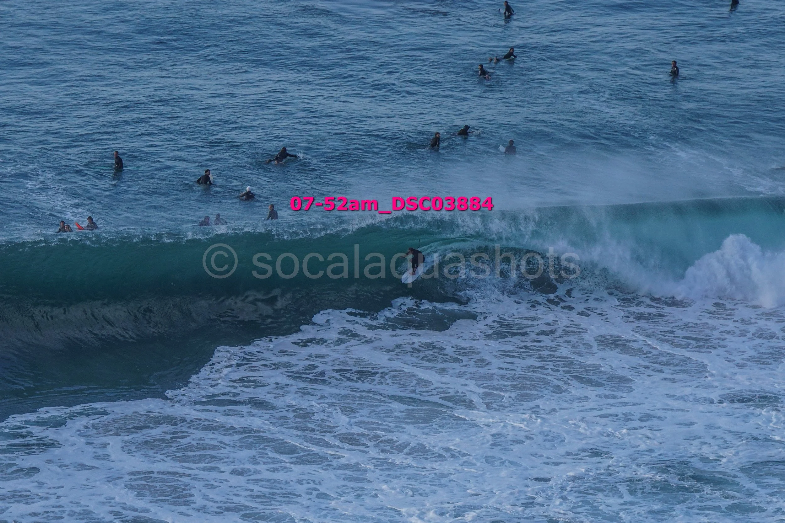People in wetsuits swimming and surfing in the ocean, with one person surfing on a wave.
