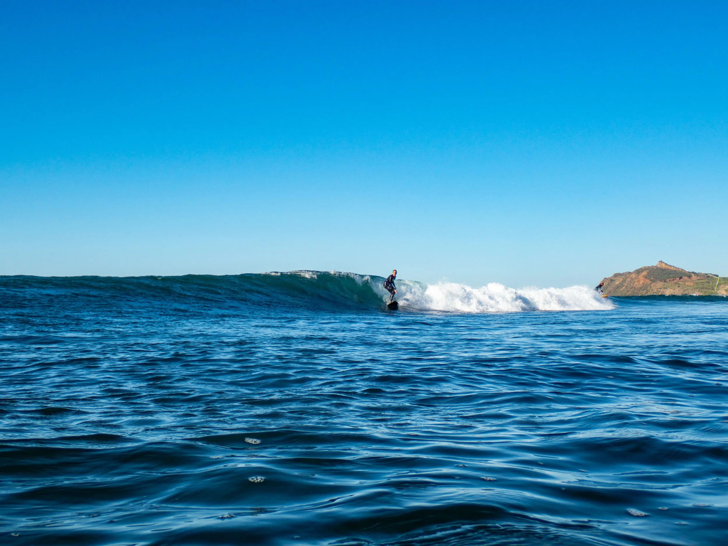 Surfer riding a wave in the ocean with a hill in the background.